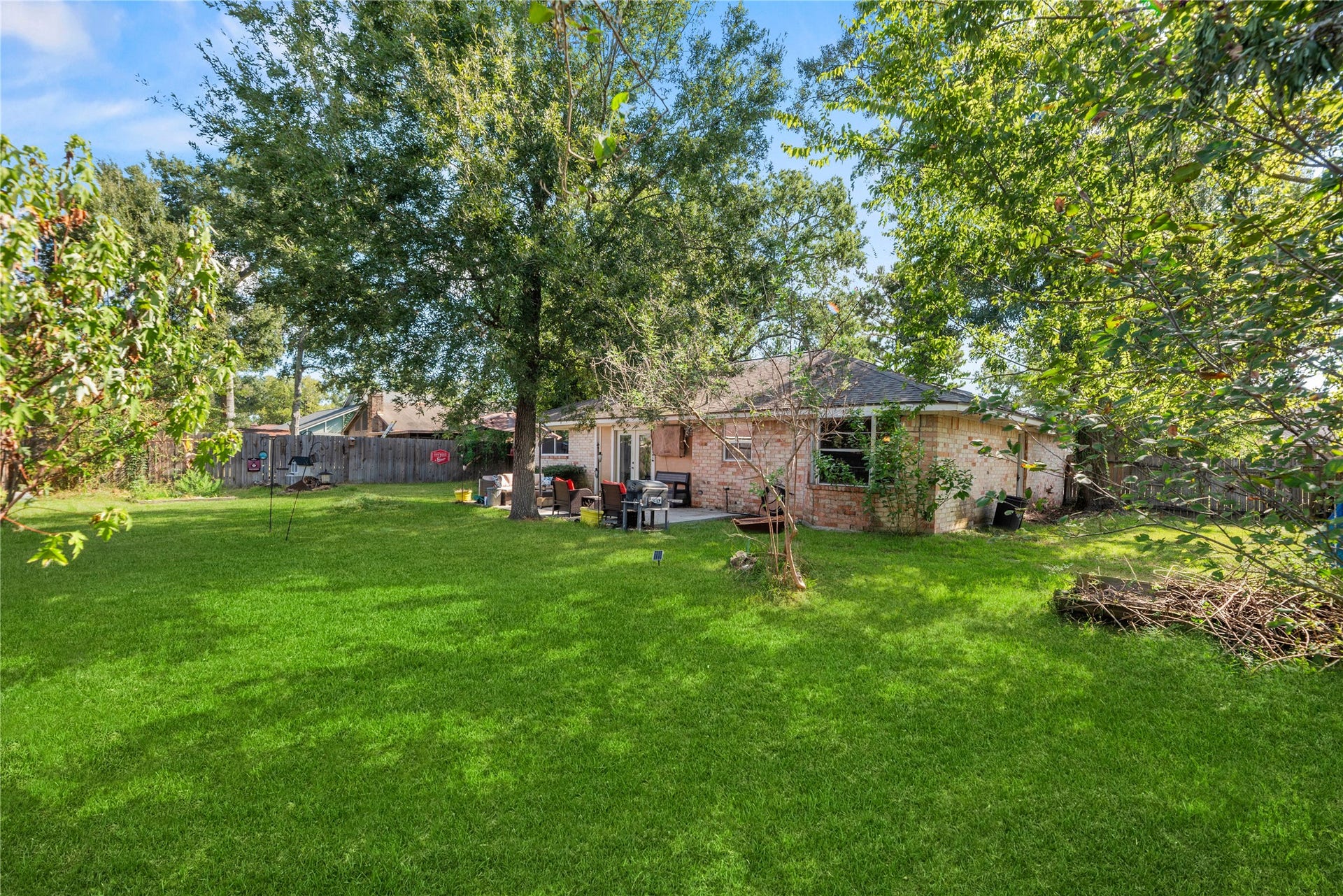 Original rear-yard perspective showing the home, mature trees, and existing yard features before virtual clearing.