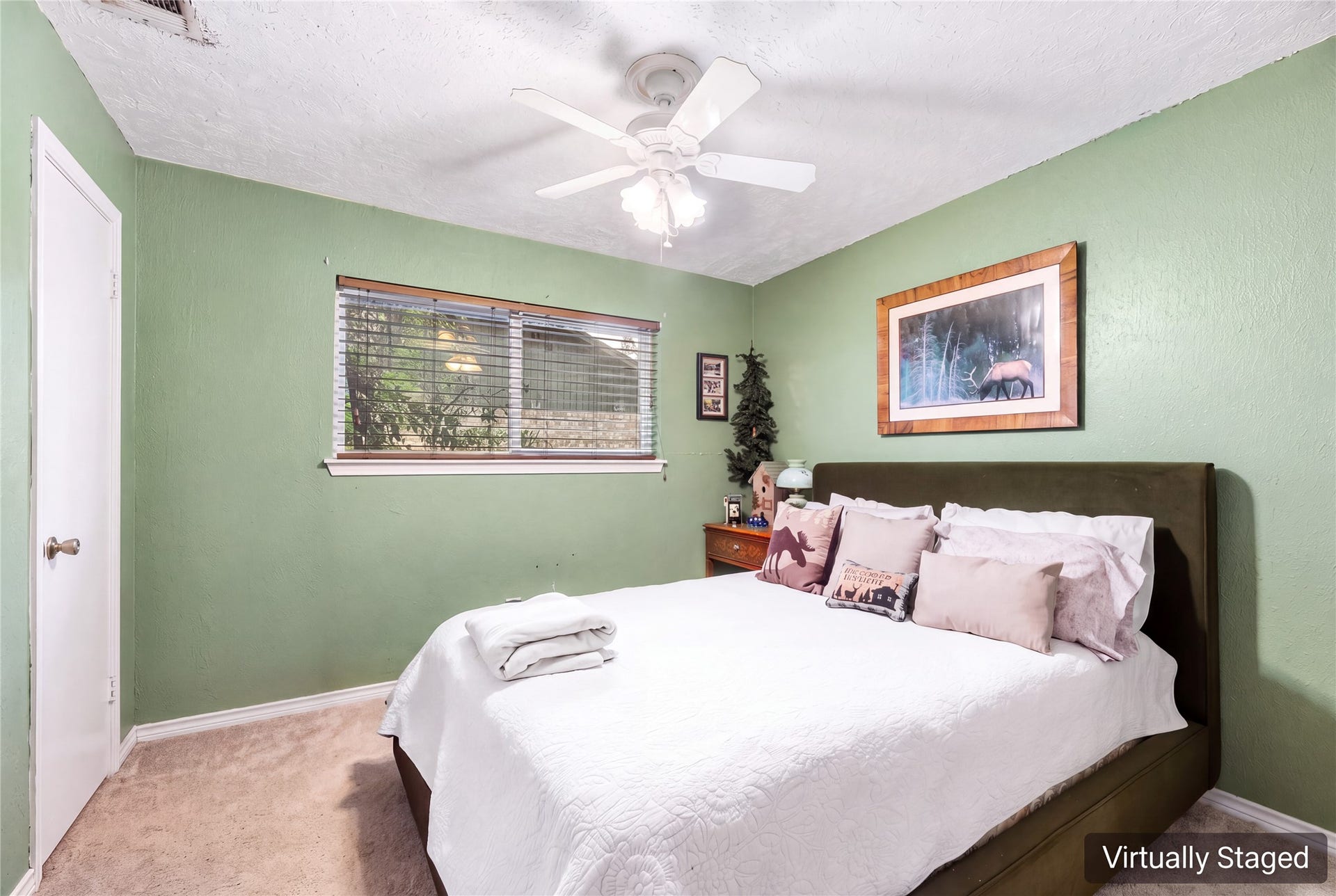Virtually staged secondary bedroom with green walls, a ceiling fan, and a window overlooking the yard.