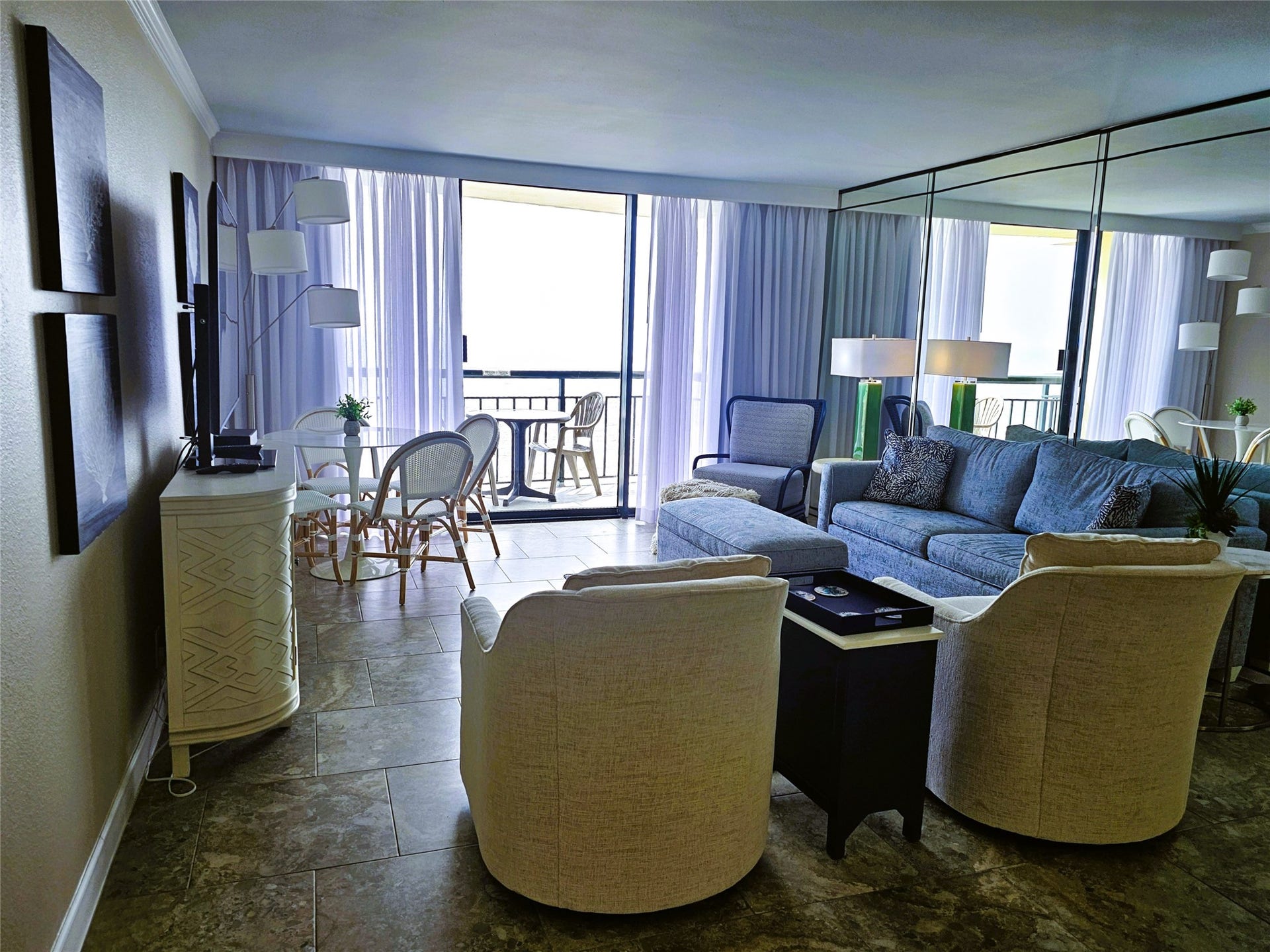 Bright and inviting living space featuring a cozy seating area, elegant tiled floors, and abundant natural light from large sliding glass doors leading to a balcony.