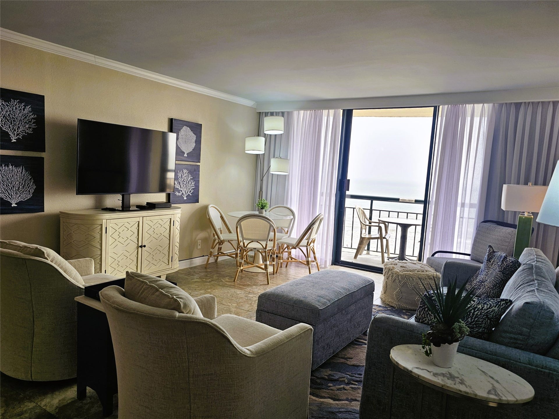 Spacious living room with modern furnishings, a large TV, and access to a balcony offering stunning ocean views.