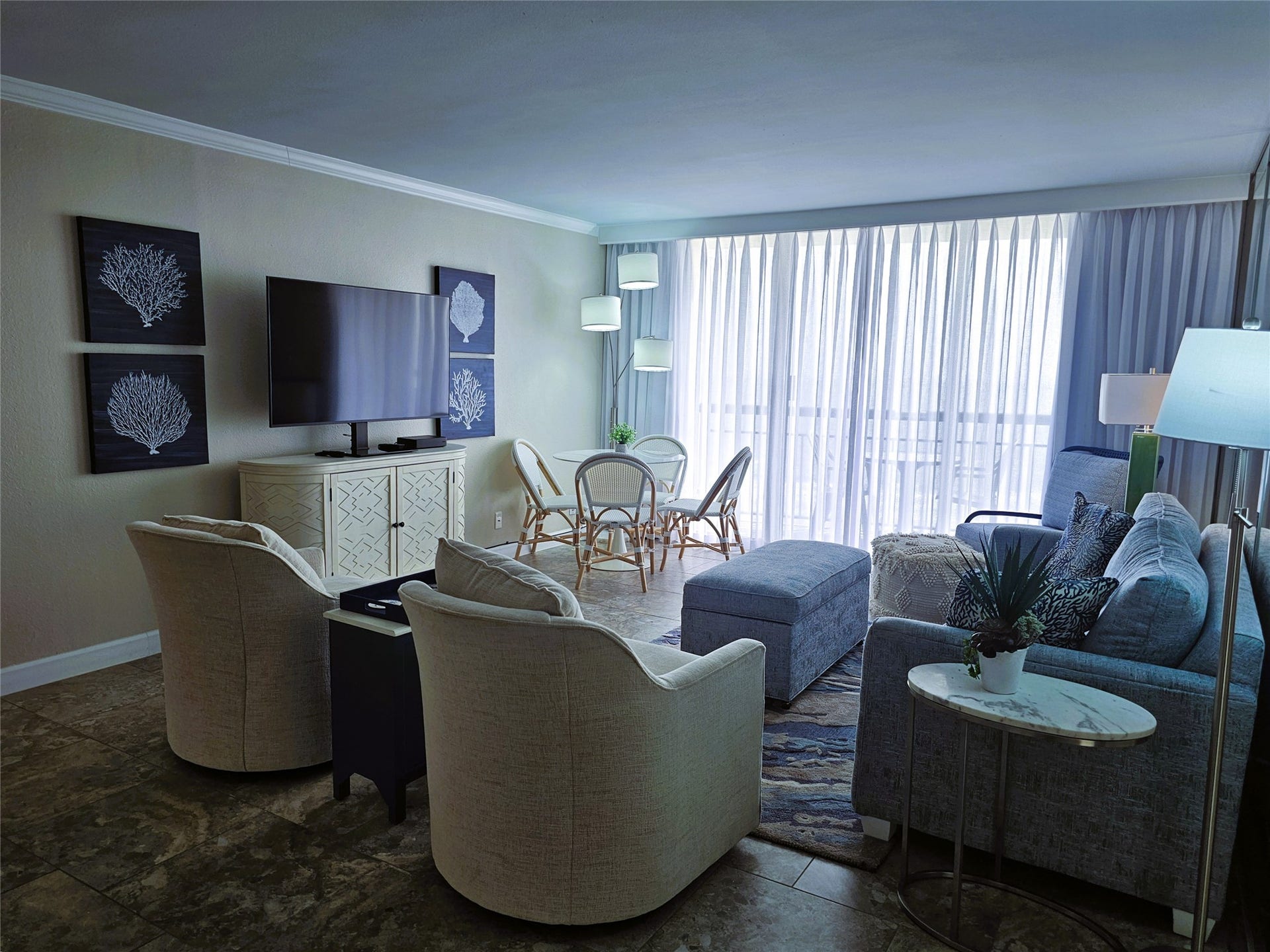 Bright and inviting living space with modern furnishings, a large flat-screen TV, and elegant decor. Floor-to-ceiling windows allow natural light to fill the room, creating a warm and welcoming atmosphere.