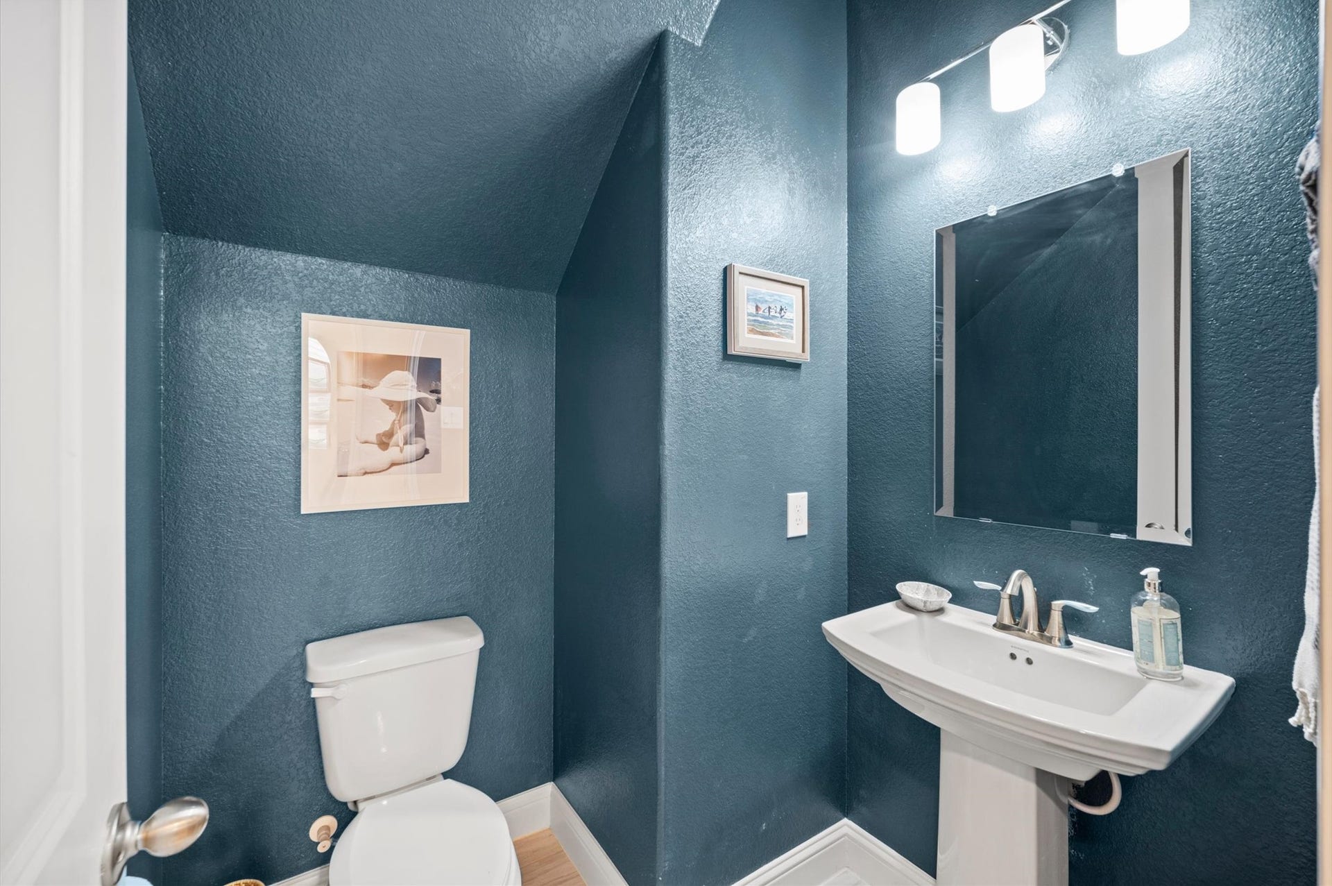 Charming powder room with elegant navy walls, a sleek pedestal sink, and modern lighting.