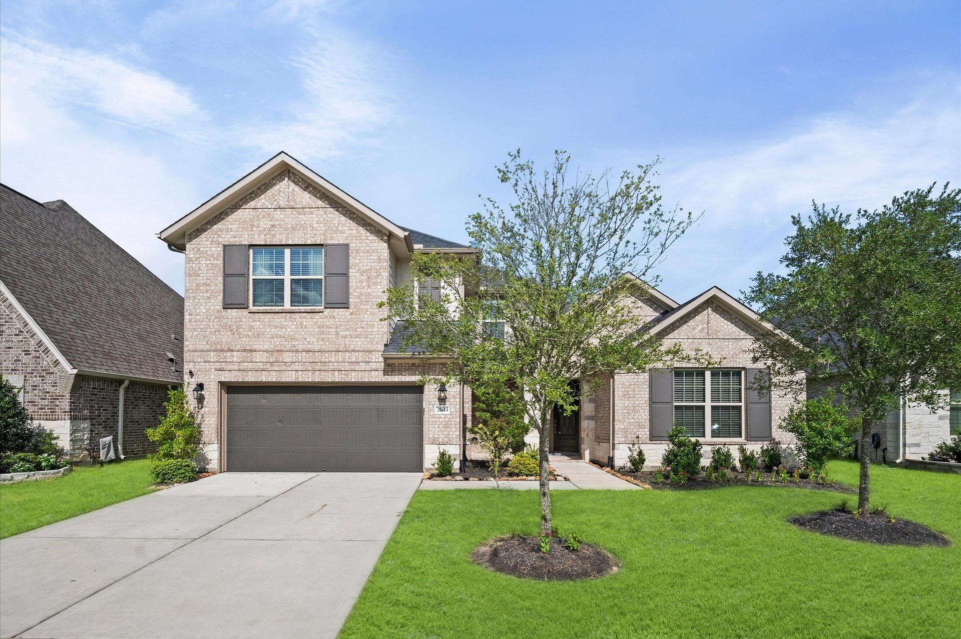 Charming two-story home with a brick exterior, featuring a spacious two-car garage and a beautifully landscaped front yard with mature trees.