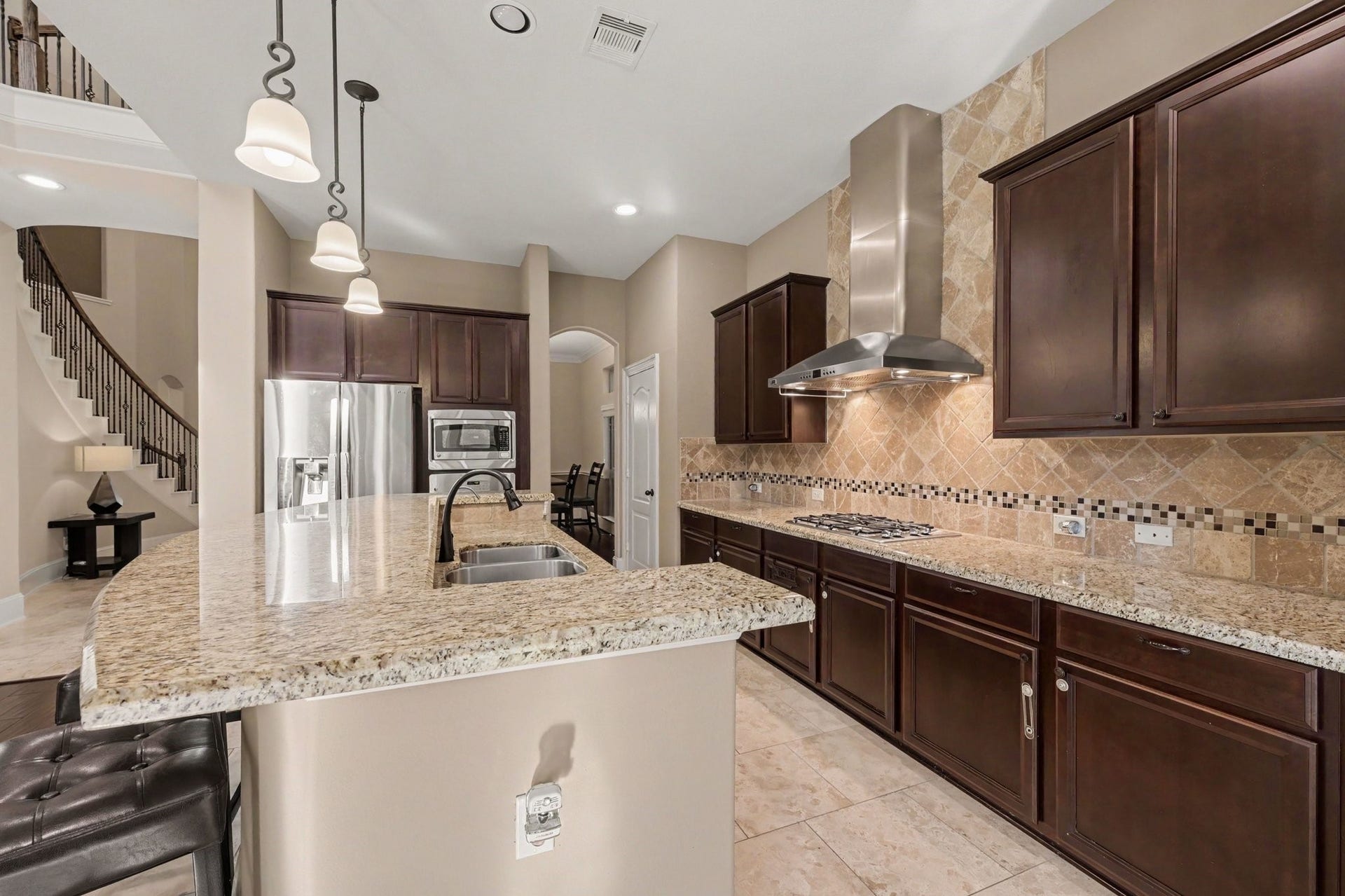 6410 Archer Ranch Lane, Rosenberg, TX 77471 Spacious open-concept kitchen featuring granite countertops, rich wood cabinetry, stainless steel appliances, a gas cooktop, and a generous breakfast bar.