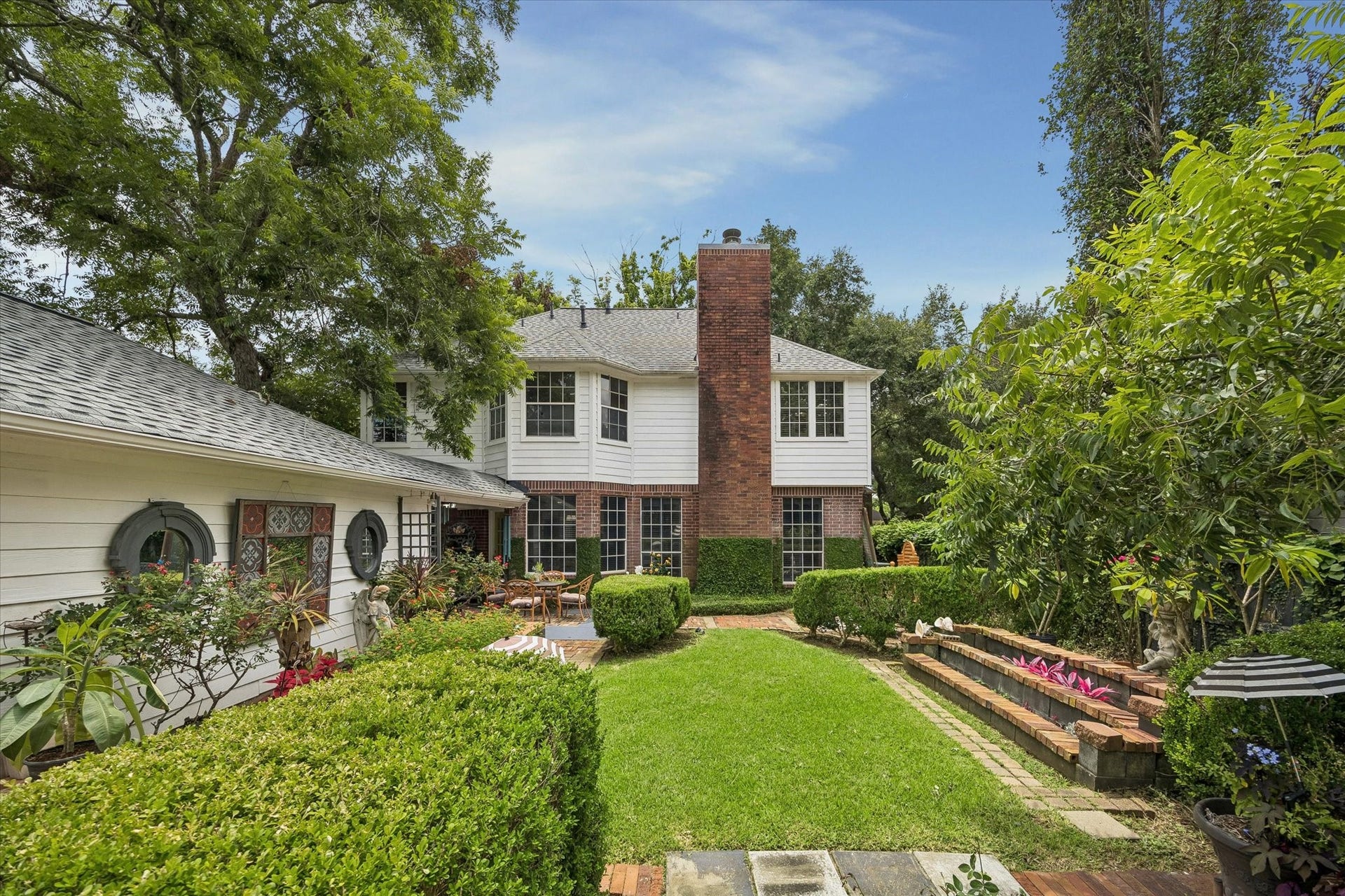 1019 Quiet Glen Court, Sugar Land, TX 77479 Charming two-story home with a classic brick chimney, surrounded by lush greenery and a manicured garden, offering a serene outdoor retreat.