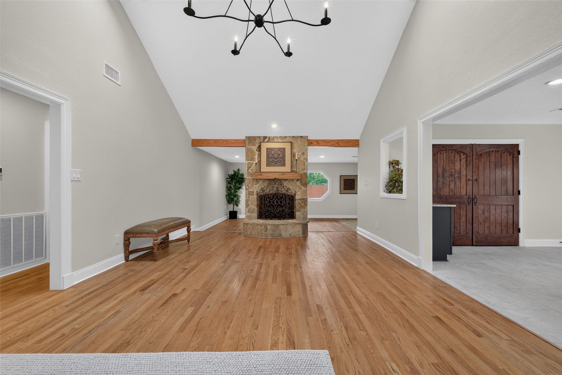 8906 Seber Drive, Tomball, TX 77375 Expansive living room with vaulted ceiling, wood floors and a striking stone fireplace. The kitchen is accessible on the right, primary and secondary bedrooms on the left. Around the fireplace is the added flex room.