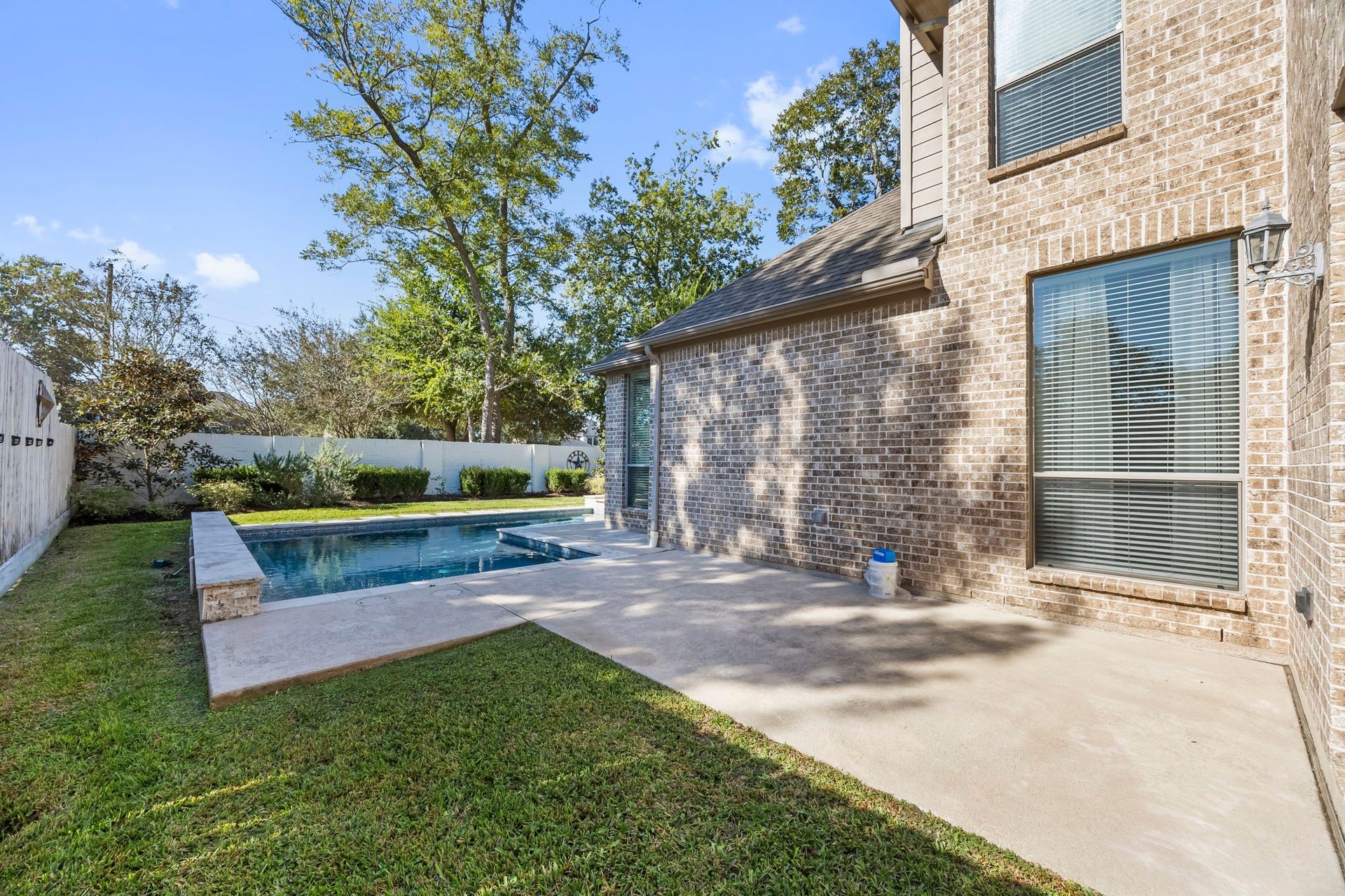 9238 Balsam Gap, Missouri City, TX 77459 Another view of the backyard highlights the additional concrete patio area, perfect for outdoor dining, grilling, or creating a second seating space. The combination of open lawn, mature trees, and poolside living offers plenty of options for enjoying the outdoors.