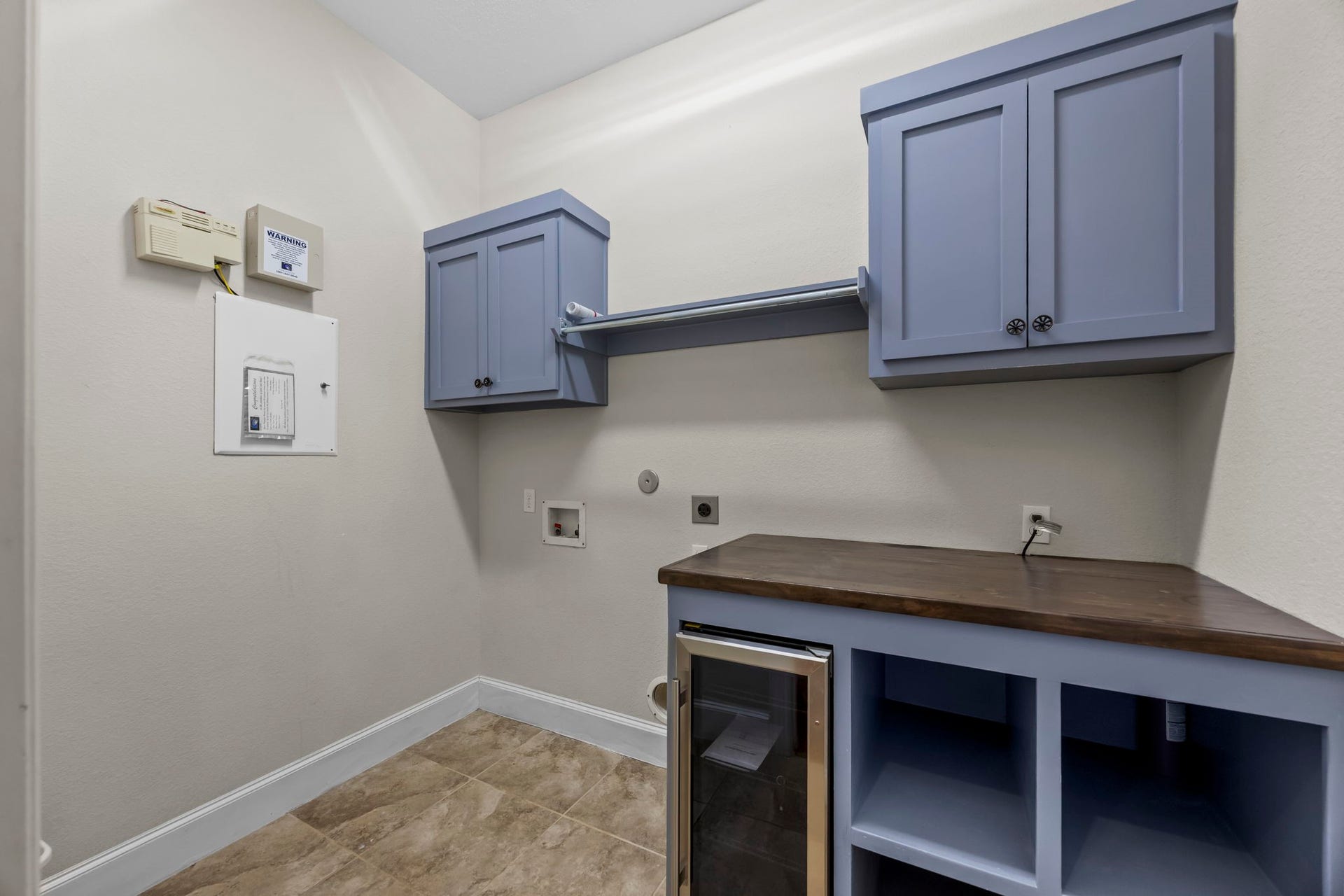 9238 Balsam Gap, Missouri City, TX 77459 Functional utility room featuring custom cabinetry, a folding countertop, open storage cubbies, and a built-in beverage refrigerator. Washer and dryer connections and additional overhead storage make this a convenient space for everyday household needs.