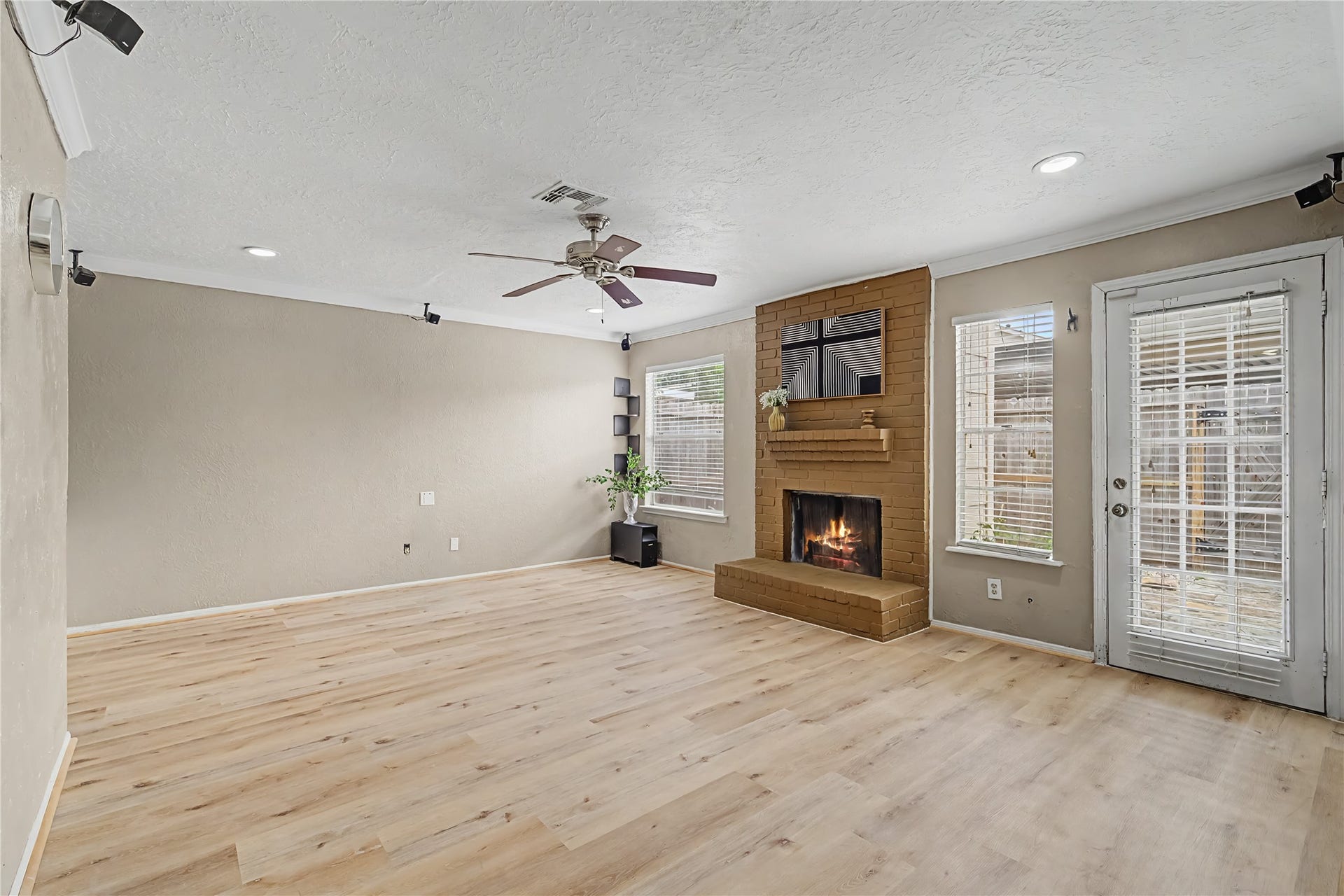 Open living space featuring a brick fireplace, built-in shelving, crown molding, and wood-look flooring.