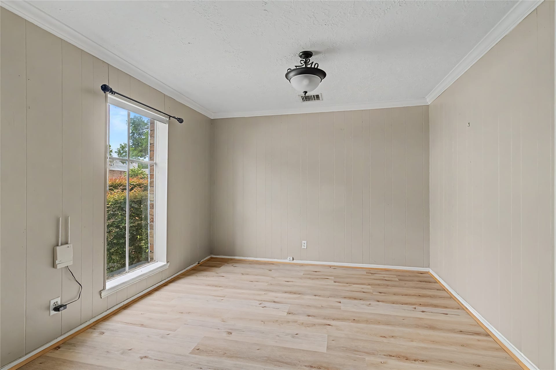 Versatile room with wood-look flooring, paneled walls, crown molding, and a large window providing natural light.