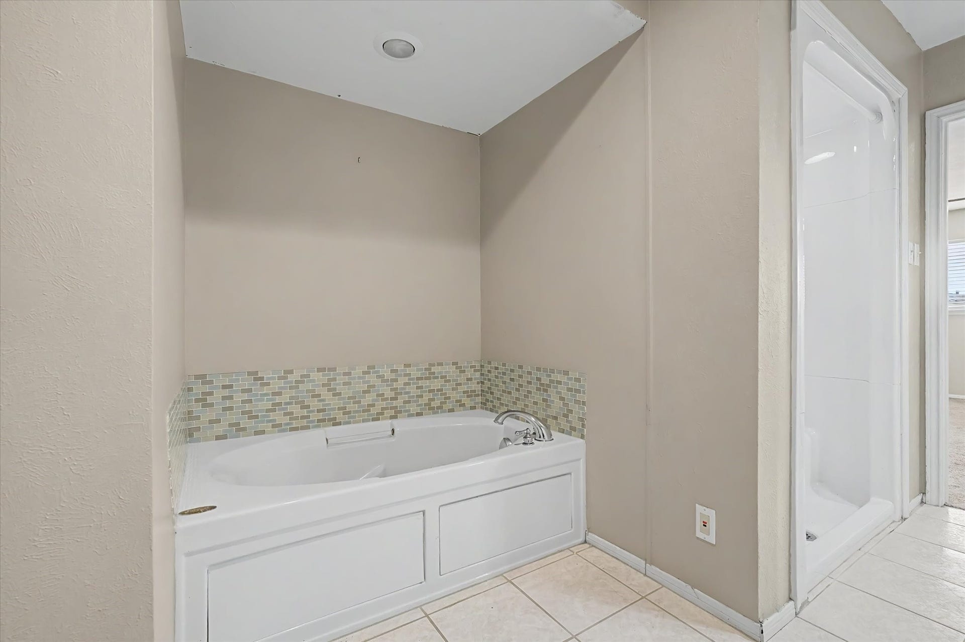 Separate soaking tub with tile accent surround and recessed lighting.