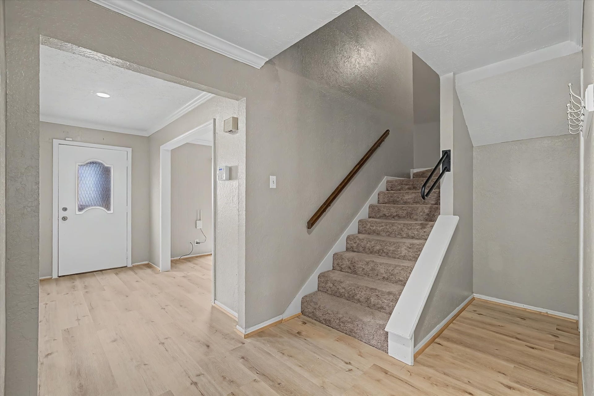 Bright entryway with wood-look flooring and carpeted staircase leading upstairs.