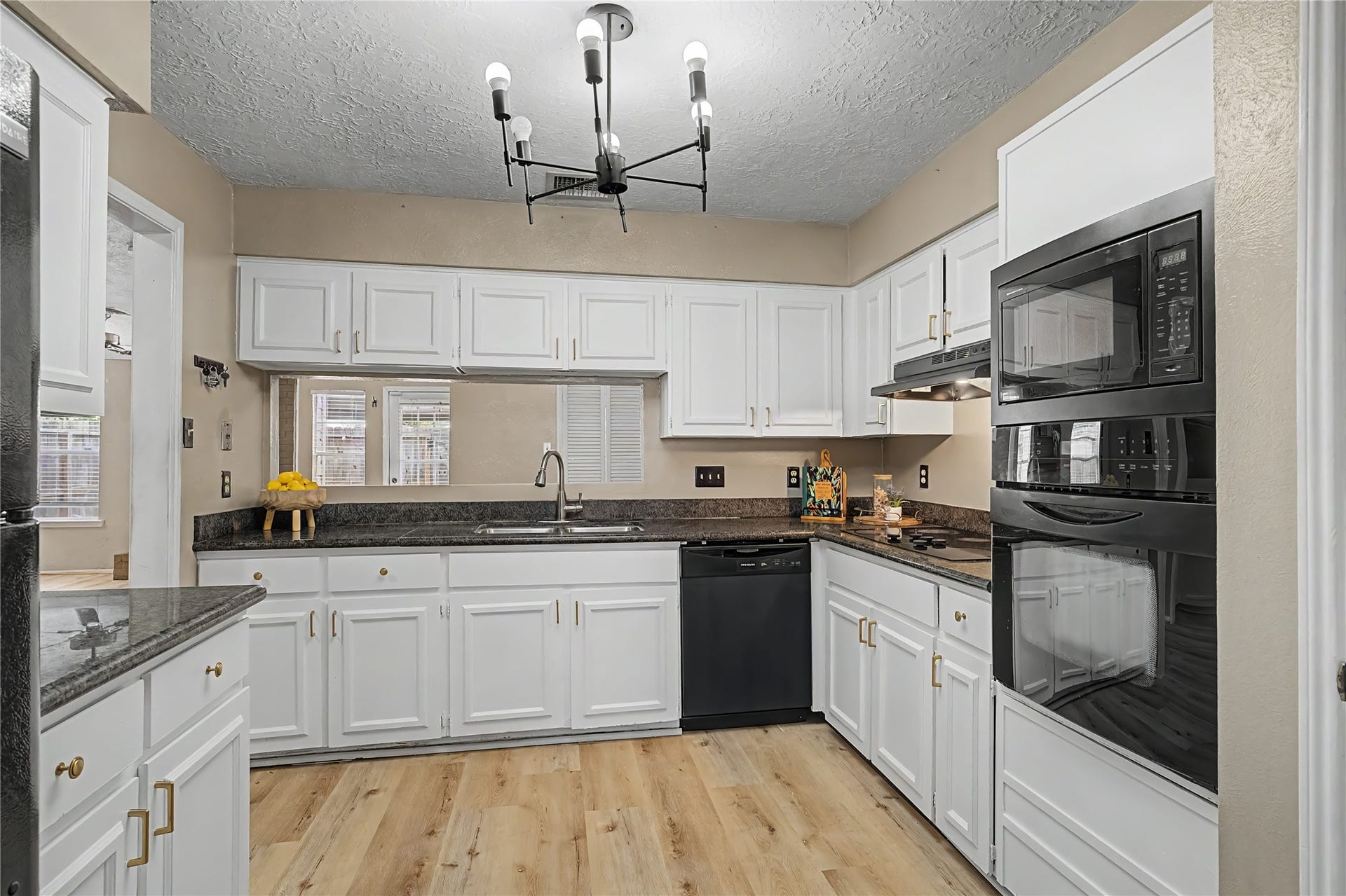 Another view of the kitchen highlighting abundant cabinetry, granite countertops, black appliances, and pass-through opening.
