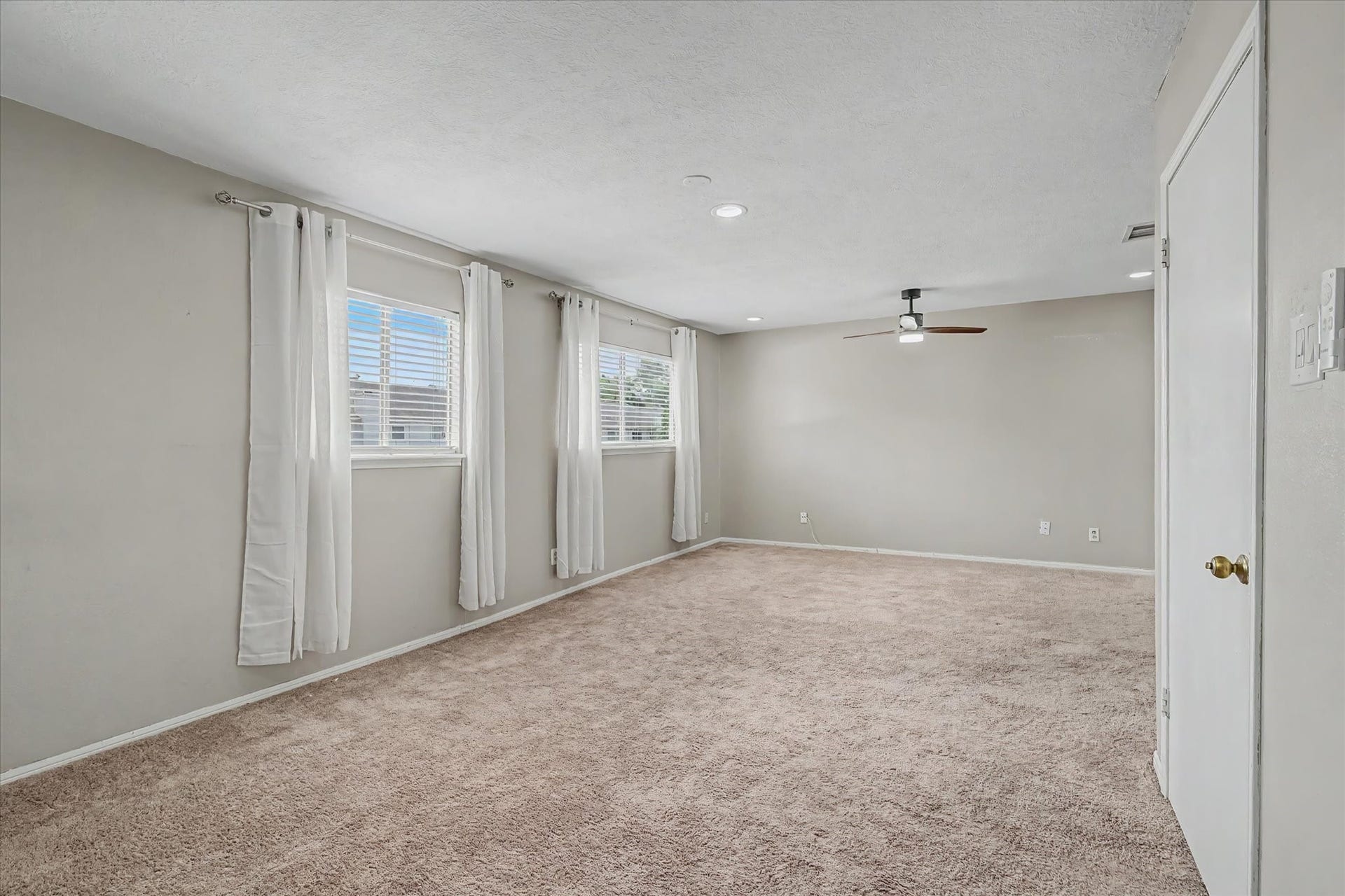 Generously sized primary bedroom with neutral carpeting, recessed lighting, ceiling fan, and multiple windows for natural light.