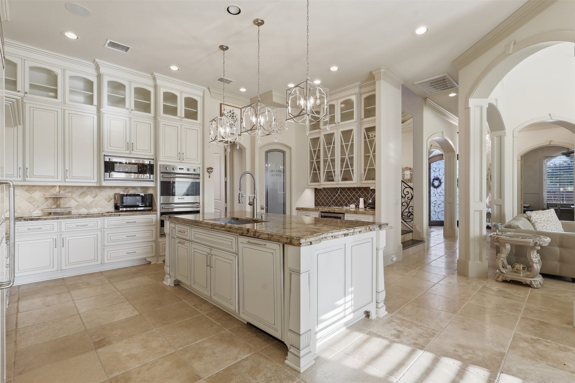 A spacious kitchen configuration features a central work island, built-in double ovens, a wet bar area with geometric tile accent, and frosted glass pantry doors.