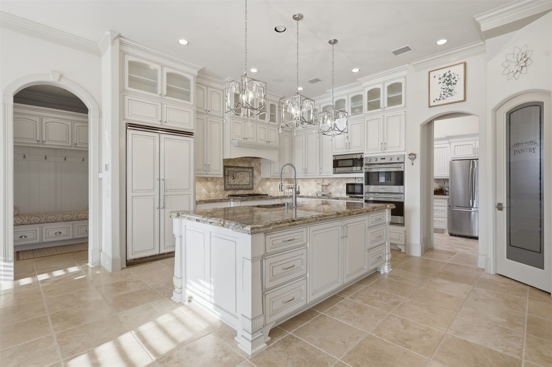 The island kitchen showcases double-stacked glazed cabinetry with glass fronts, granite counters, a tumbled stone backsplash, and lantern pendant lighting.