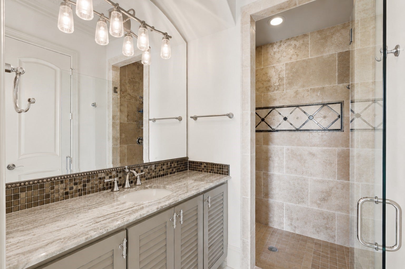 Bedroom 2 ensuite bath with a stone-top vanity, mosaic tile backsplash, and frameless glass shower.