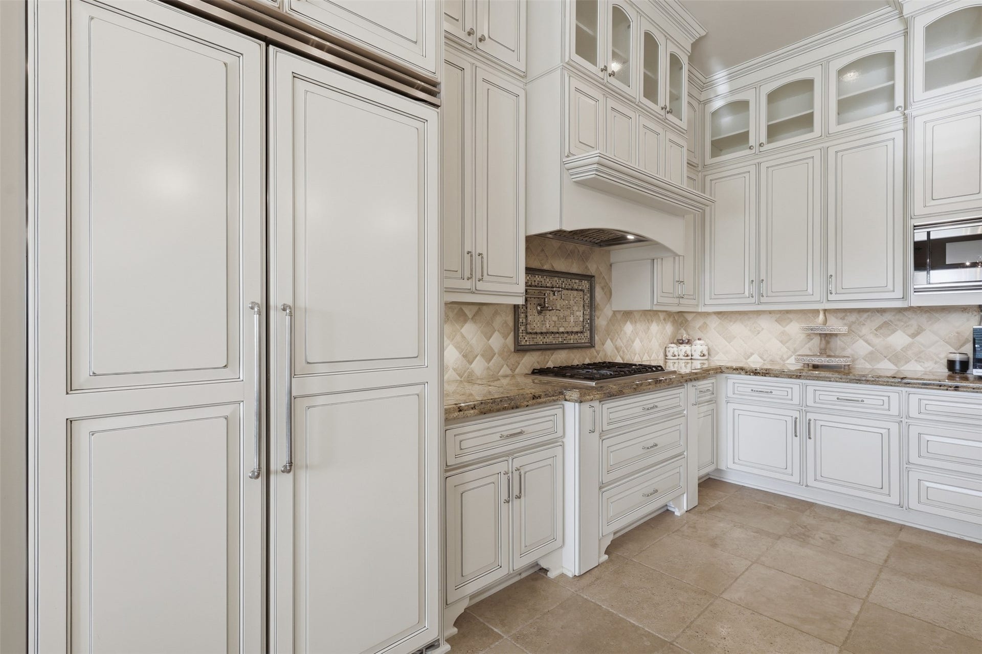 Custom panel-front refrigeration integrates seamlessly into full-height cabinetry surrounding a gas cooktop with a plaster range hood and pot filler tap.