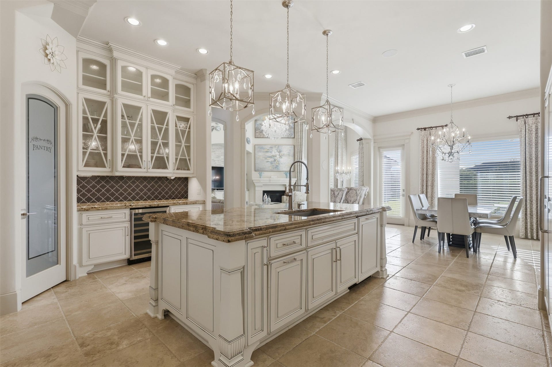 An open chefs kitchen extends into an informal dining area, accented by a dry bar with wine refrigeration, polished countertops, and recessed lighting.
