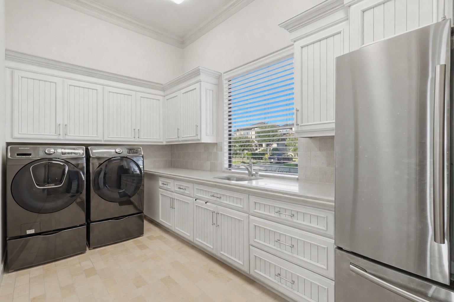 The utility room features extensive beadboard cabinetry, solid-surface countertops with an integrated sink, crown molding, and stone tile flooring.