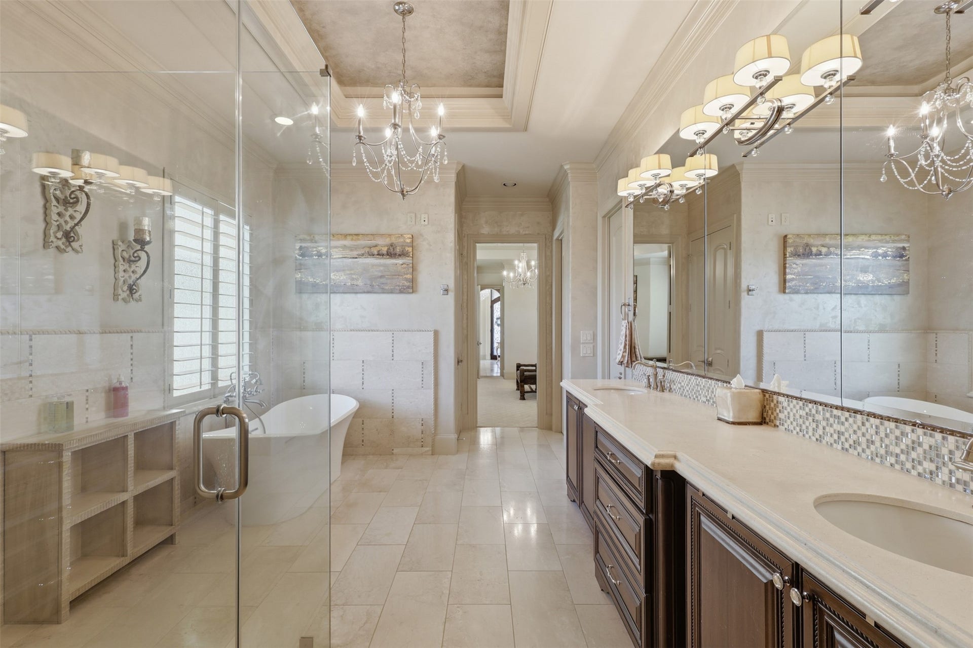 Another angle of the primary bath highlights dual undermount sinks, rich wood cabinetry, a mosaic tile backsplash, full-wall mirrors, and stone tile flooring.