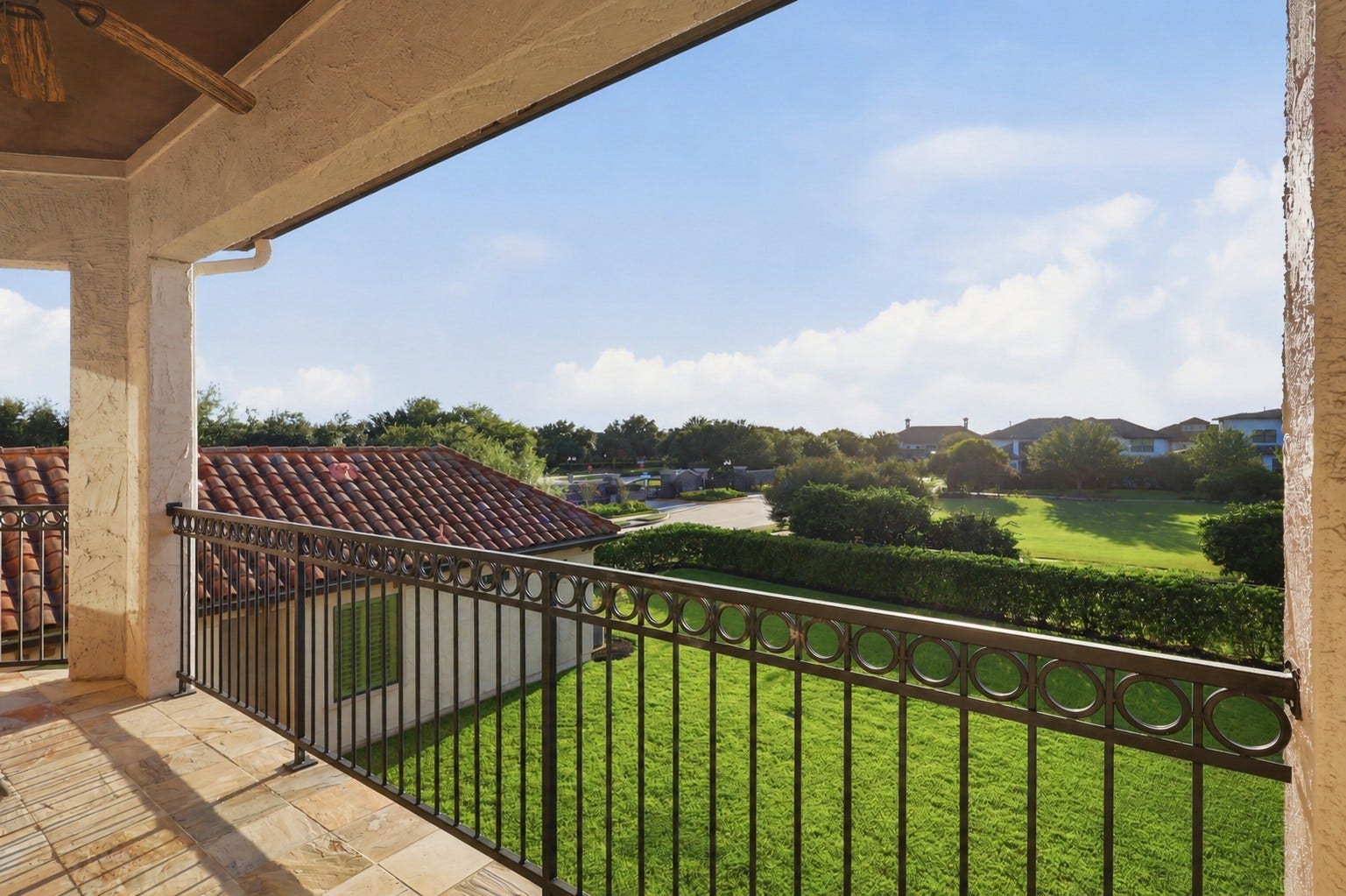 Covered second-story balcony featuring stone-tiled flooring, a stained wood ceiling, and wrought-iron railing overlooking the grounds and surrounding neighborhood.