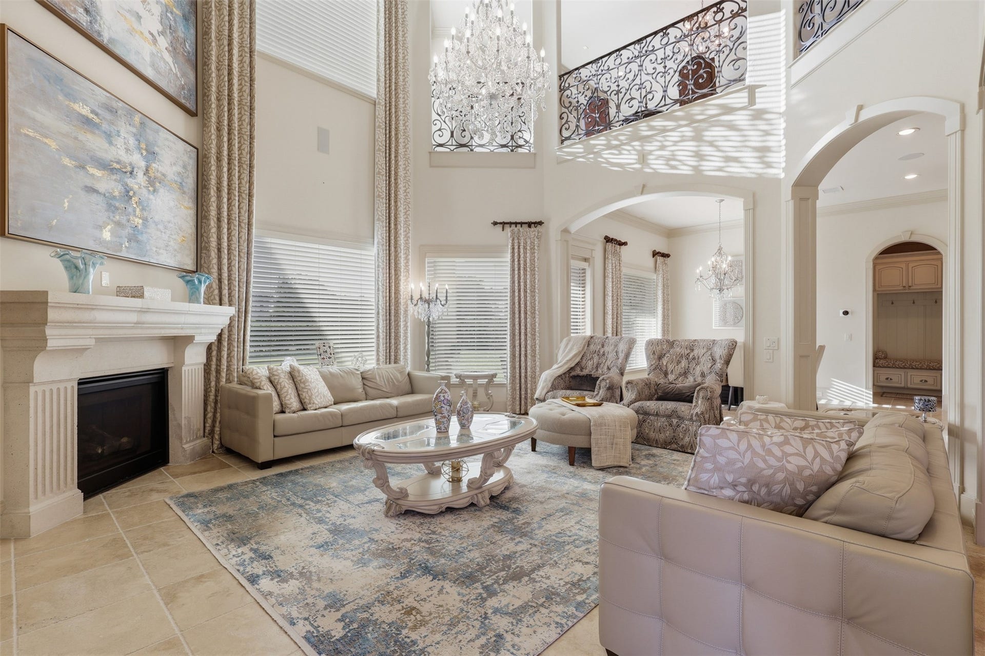 A two-story living room offers a stone mantle fireplace, stacked floor-to-ceiling windows, and wrought-iron balcony railings overlooking the main level.