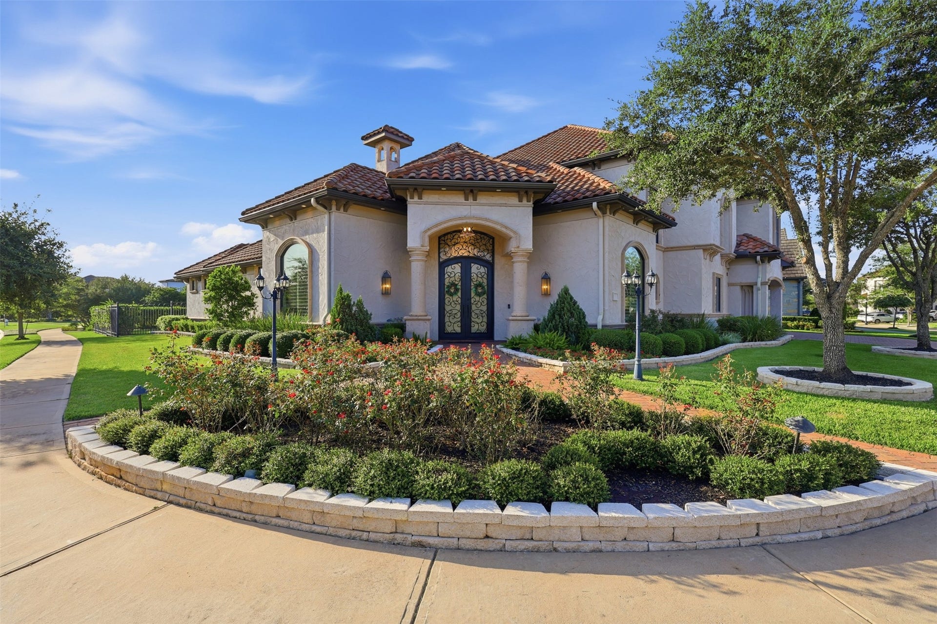 The Mediterranean exterior features stucco finishing, barrel tile roofing, arched accent windows, and integrated stone-lined garden beds along a brick paver pathway.