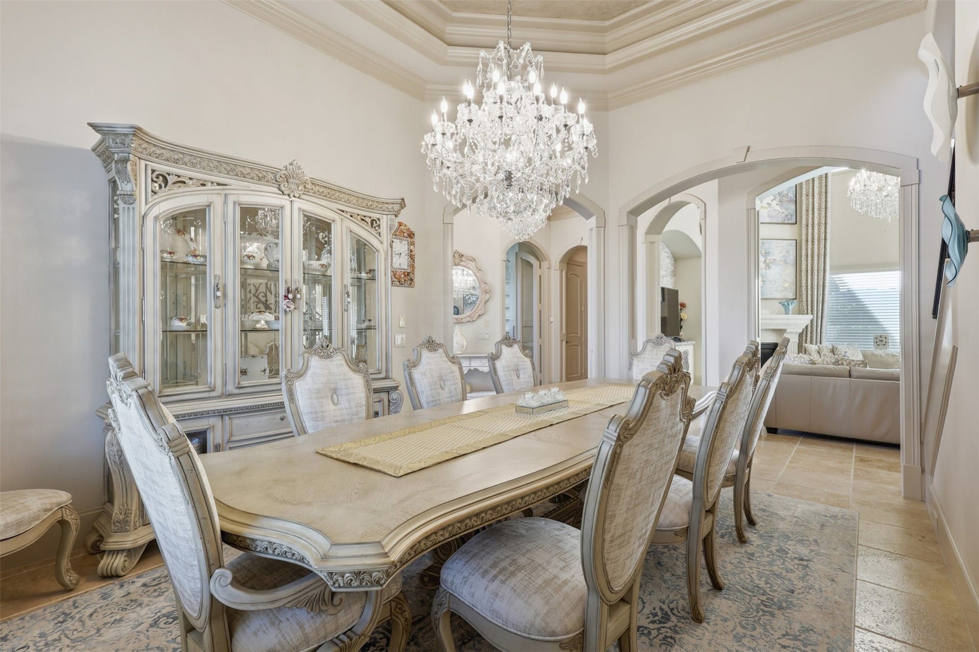 An expansive dining layout is bounded by framed arched openings, detailed ceiling trim, and travertine tile flooring running throughout the surrounding hall passageways.