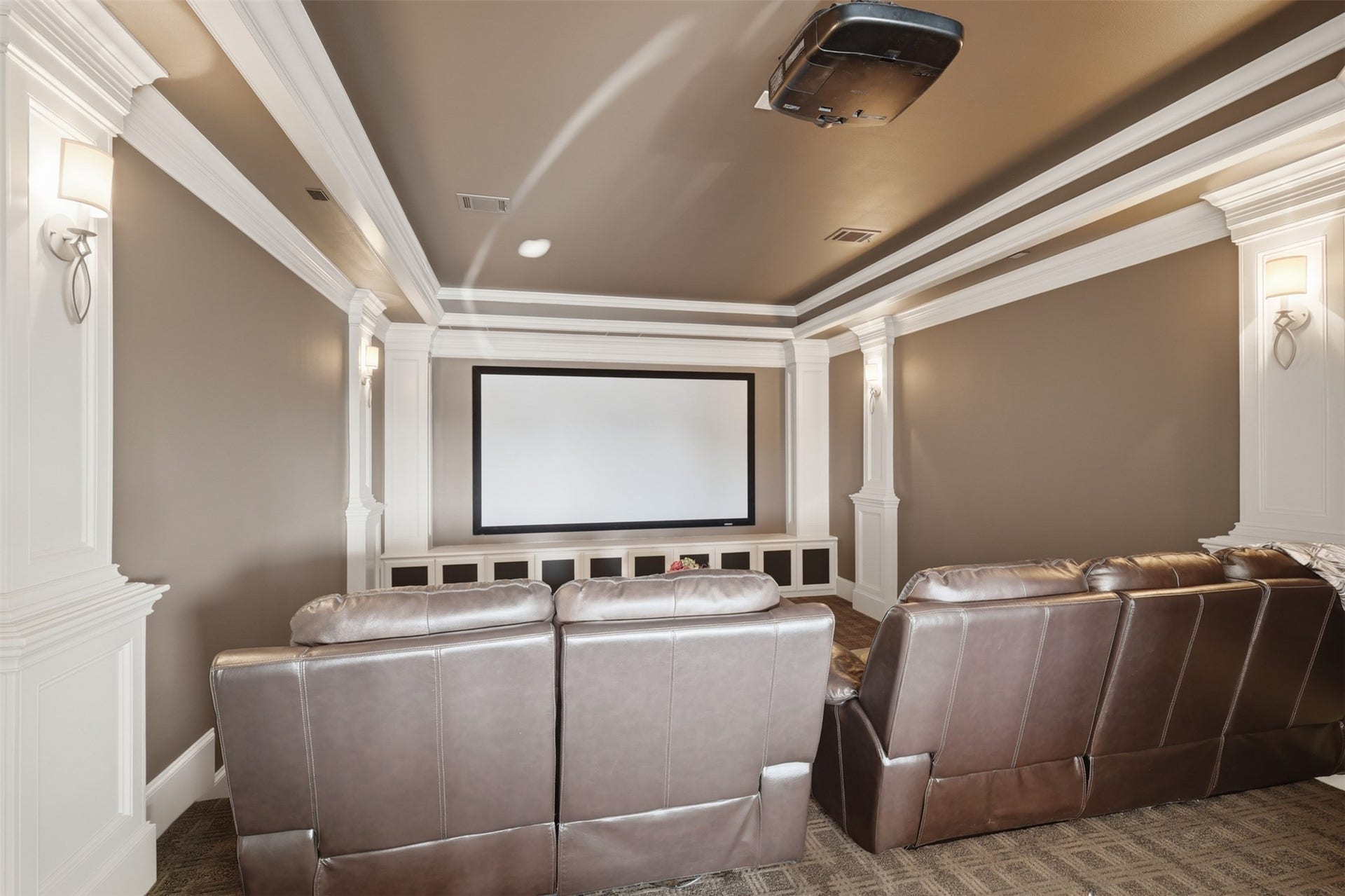 Dedicated media room enhanced by custom cabinetry, elegant wall wainscoting, crown molding, and theater-style sconce lighting.