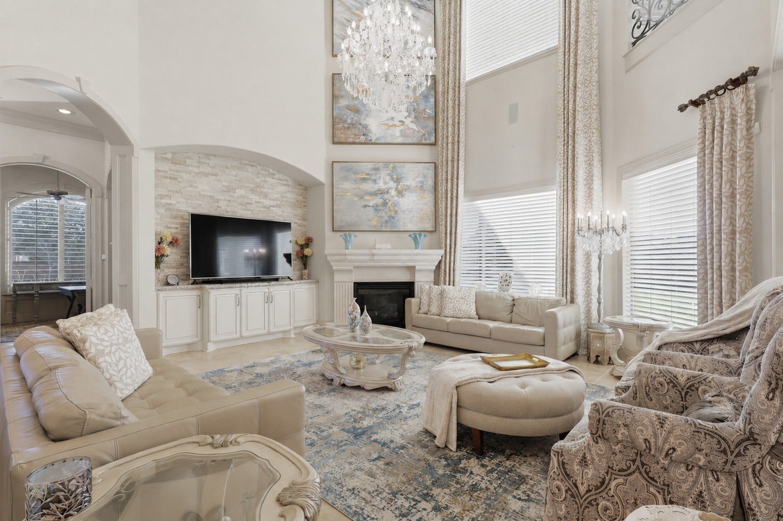 The light-filled family room centers around a stone-surround fireplace with a customized alcove, framed by double-height windows and arched passages.