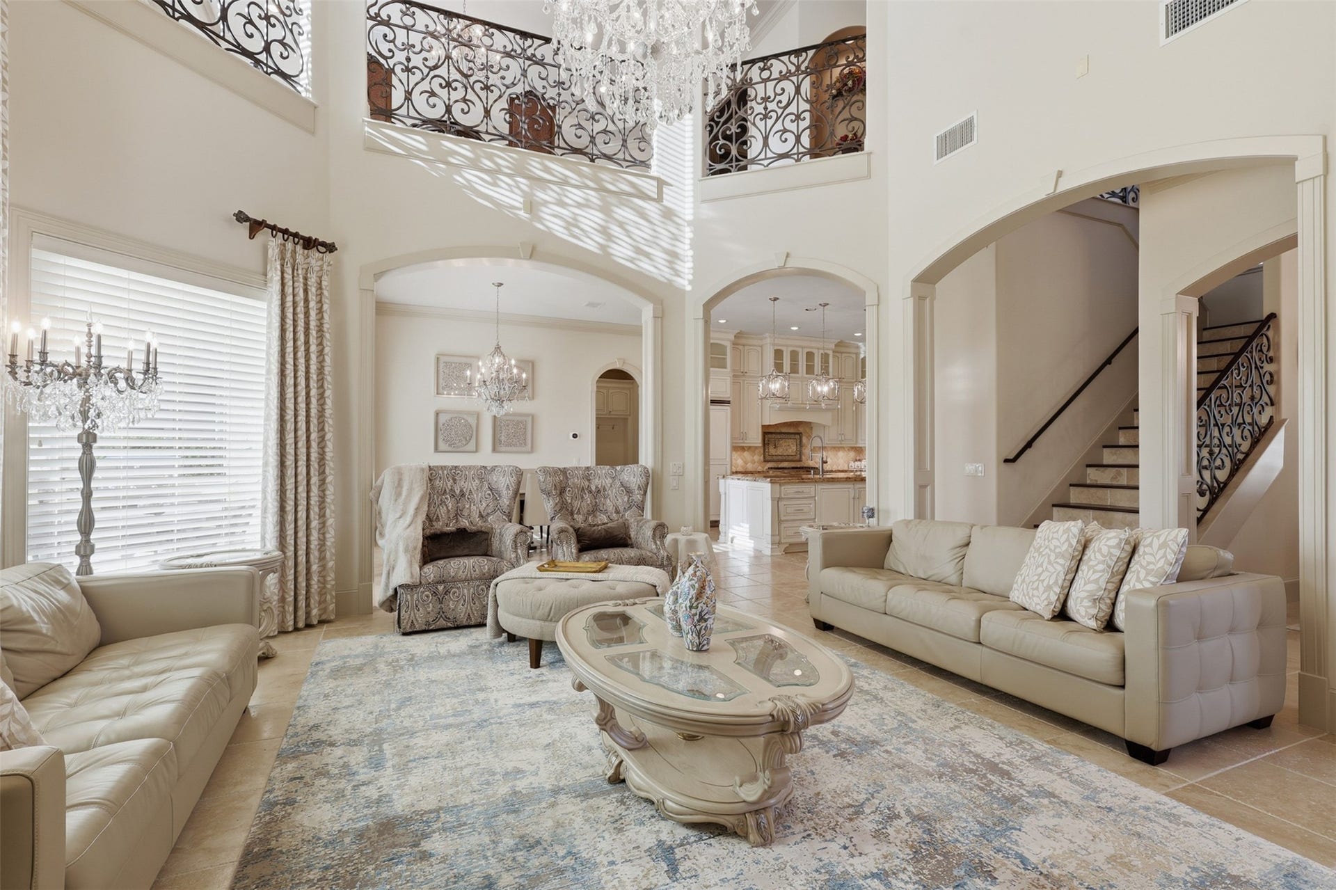 A soaring open-concept layout displays wrought-iron catwalk railings, wide-cased transition arches, and travertine tile flooring throughout.