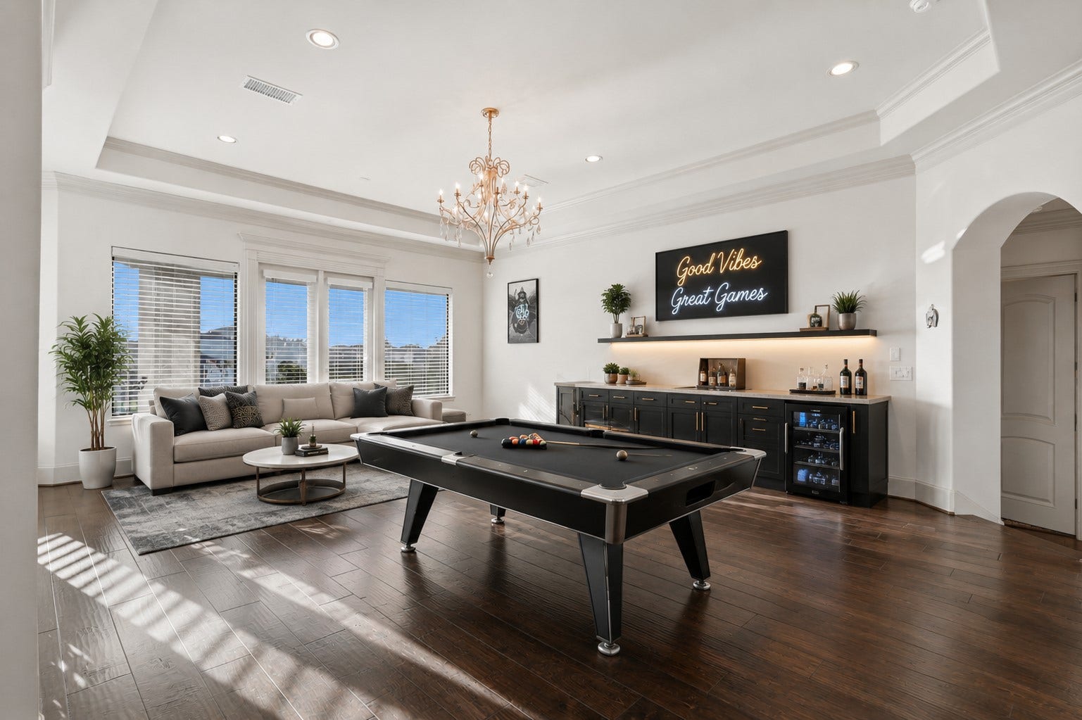 Rich hardwood flooring, a tiered ceiling with a central chandelier, and a built-in wet bar with stone counters define this space.**Virtually staged