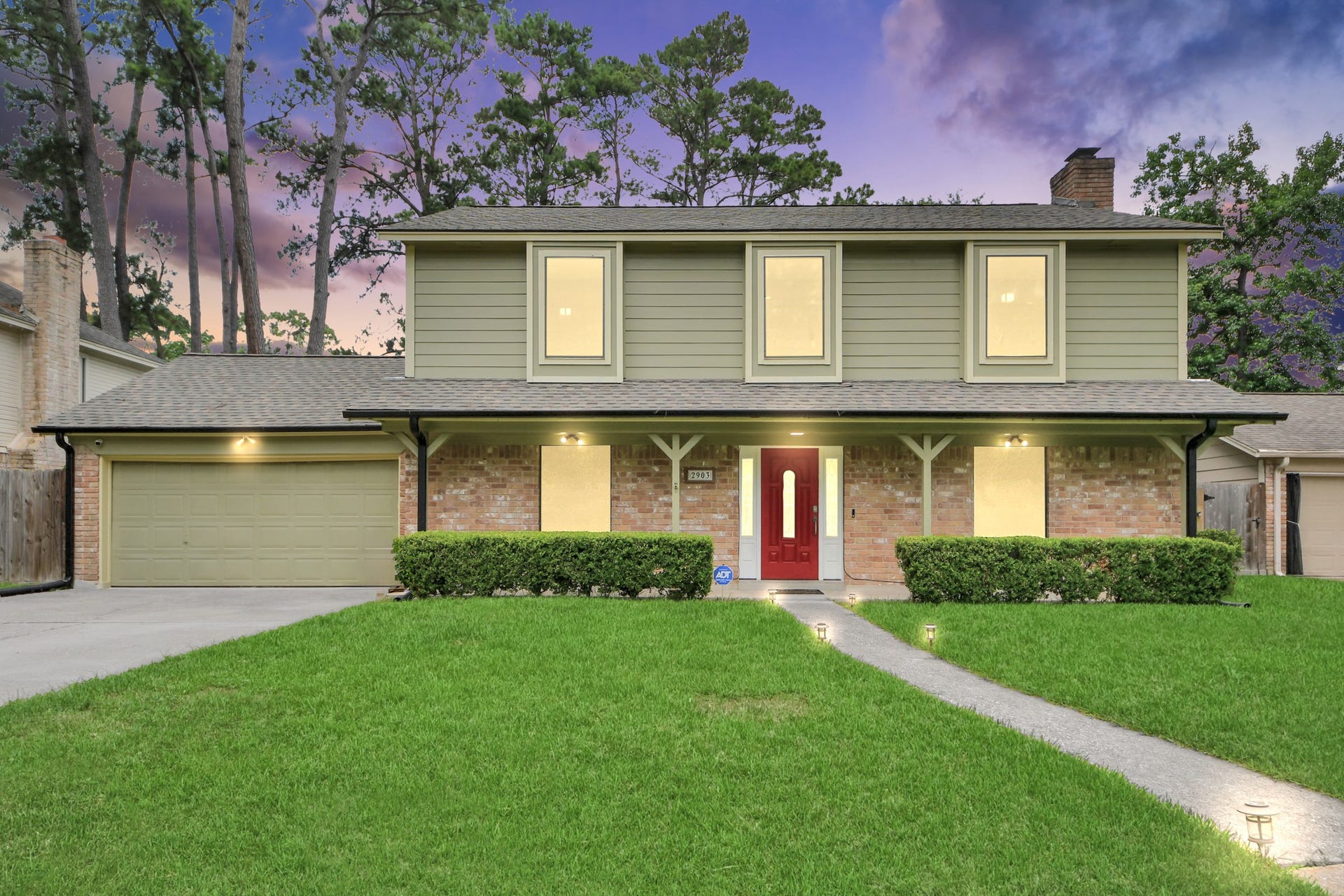 2903 Blue Glen Lane, Houston, TX 77073 An enchanting evening welcome. Captured at twilight, the glowing windows cast a warm radiance across the classic brick and cement board facade, accented by a striking red front door and a beautifully manicured, expansive lawn.