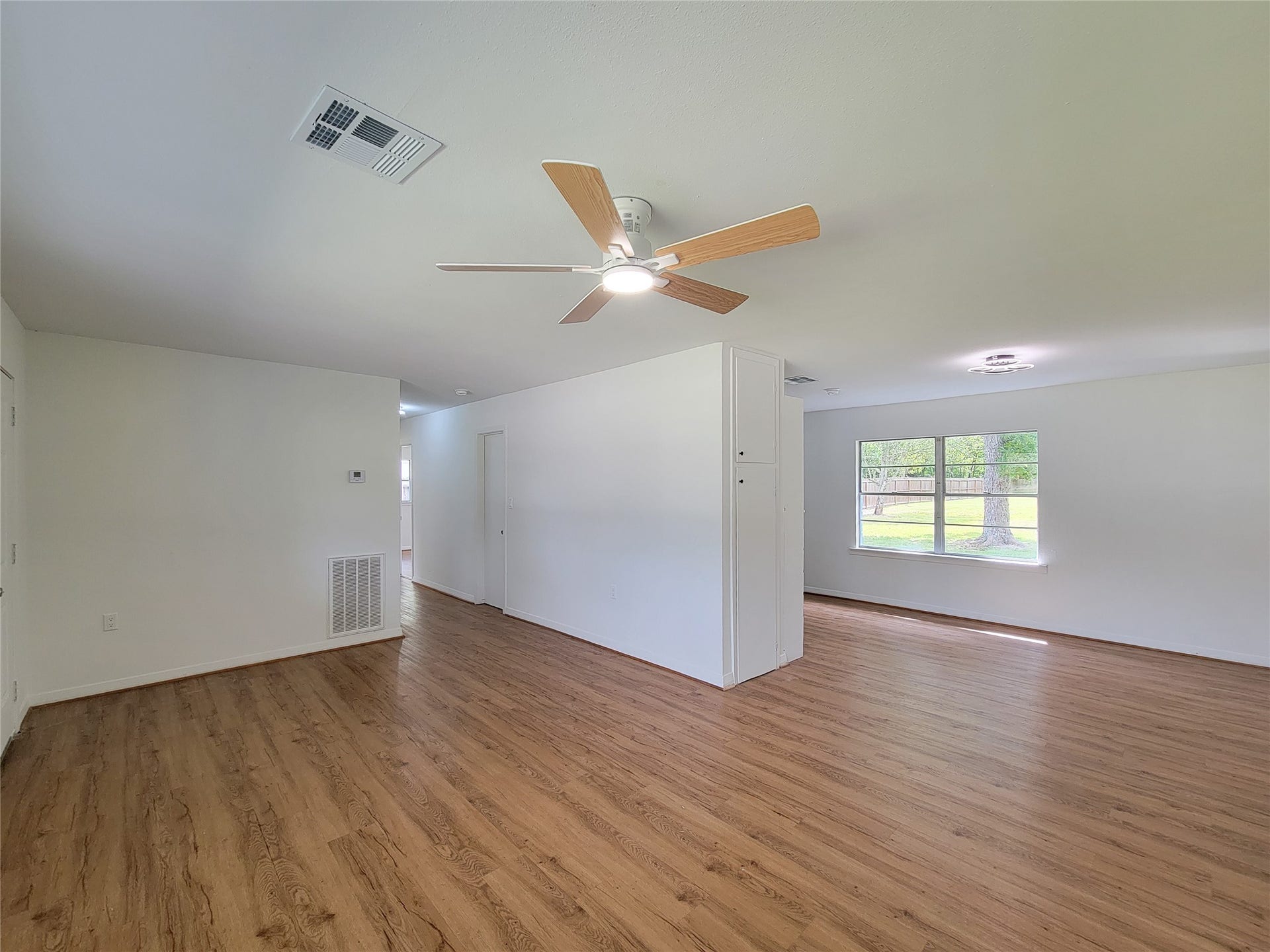 2605 W Dumble Street, Alvin, TX 77511 Discover a spacious living area with elegant wood flooring, abundant natural light from large windows, and a modern ceiling fan for ultimate comfort.