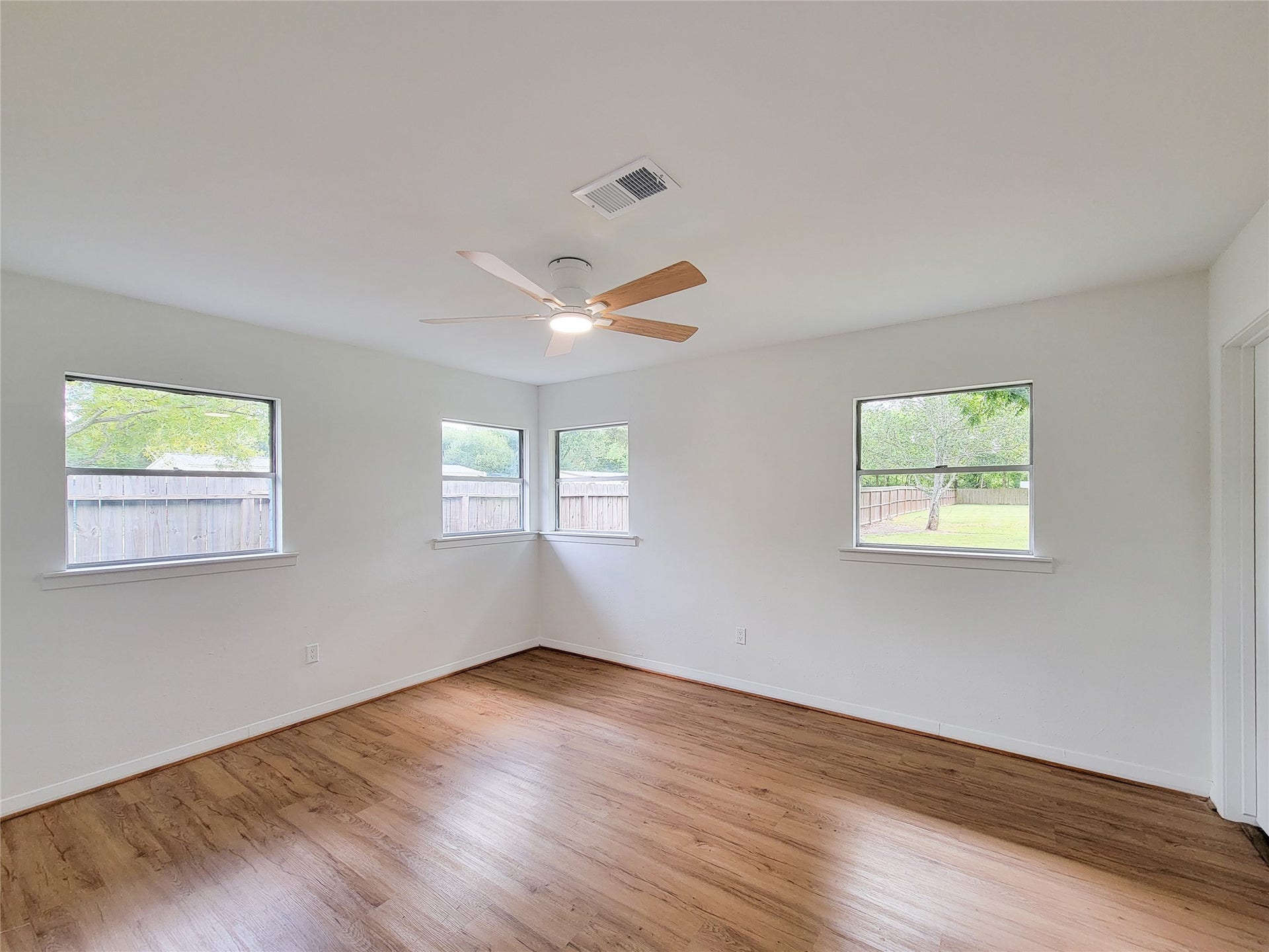 2605 W Dumble Street, Alvin, TX 77511 A bright and airy room featuring large windows, beautiful wood flooring, and a modern ceiling fan, all offering a serene view of the backyard.