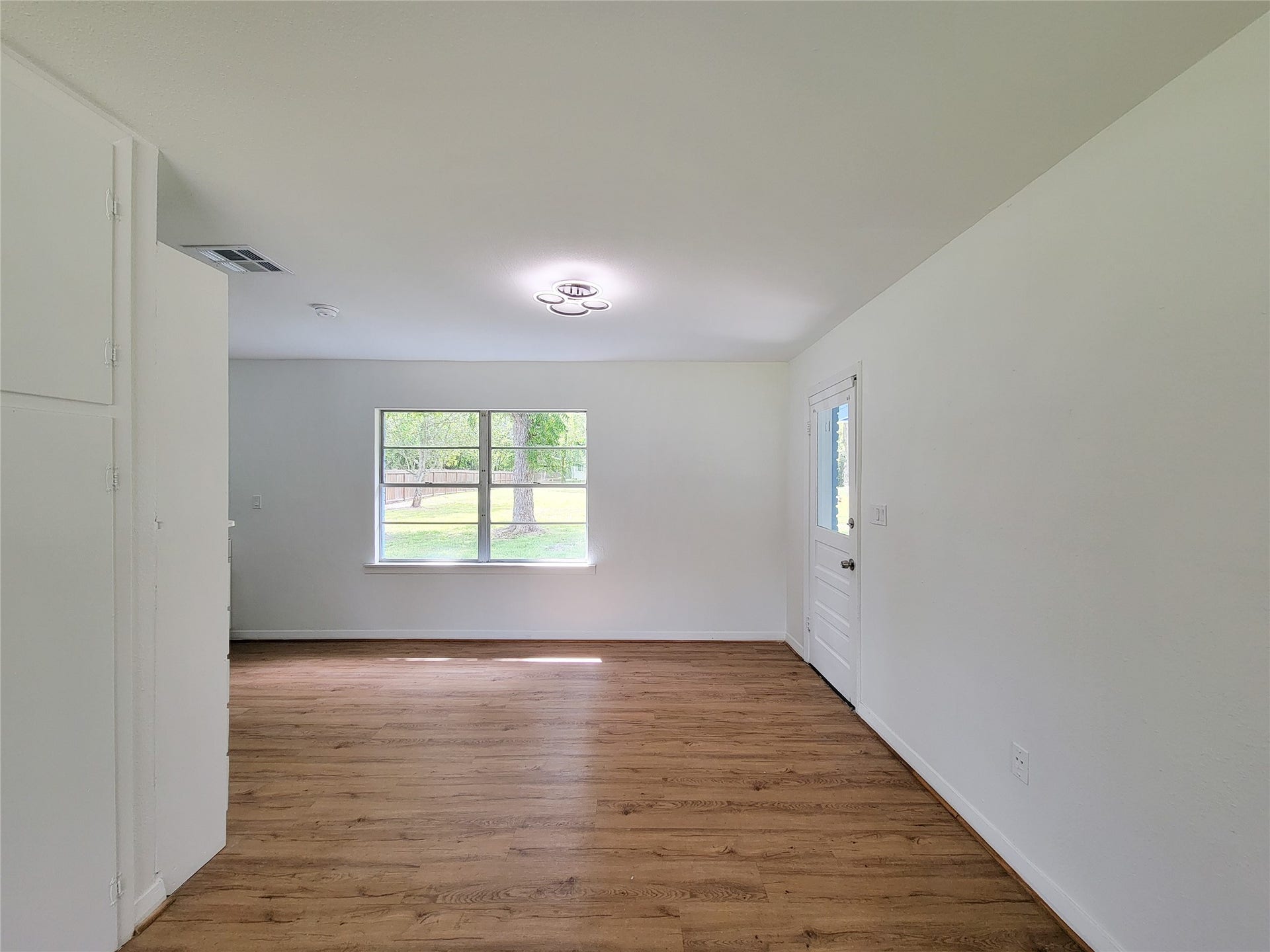 2605 W Dumble Street, Alvin, TX 77511 Experience the perfect blend of tranquility and style in this bright living area, featuring fresh white walls, warm wood flooring, and a large window framing serene outdoor views.