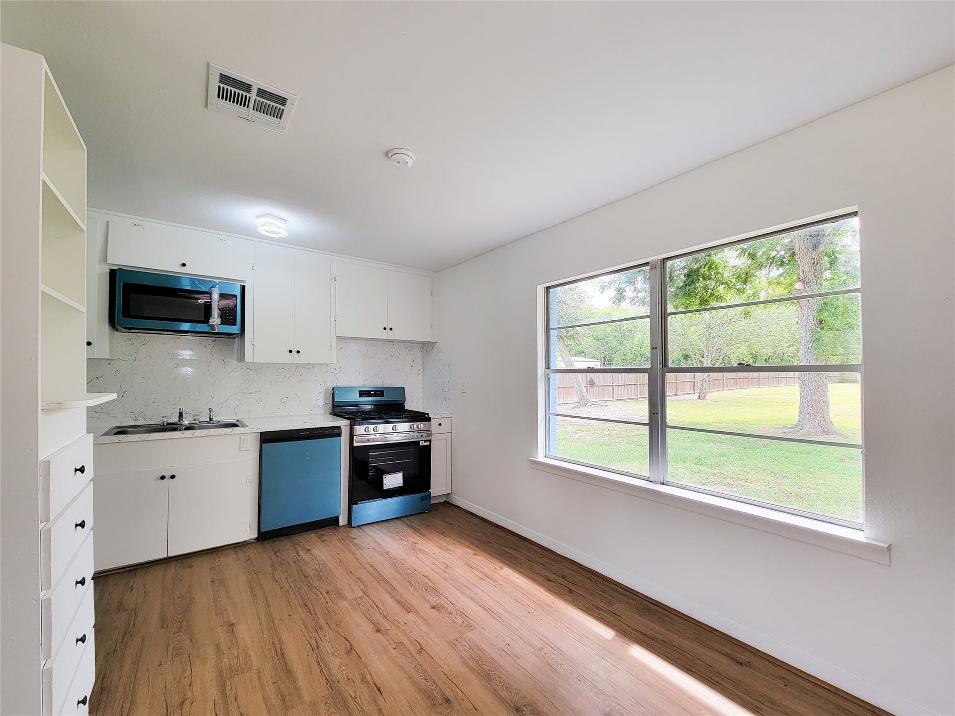 2605 W Dumble Street, Alvin, TX 77511 Bright and inviting kitchen featuring modern appliances and sleek white cabinetry, enhanced by large windows with serene views of the expansive backyard.