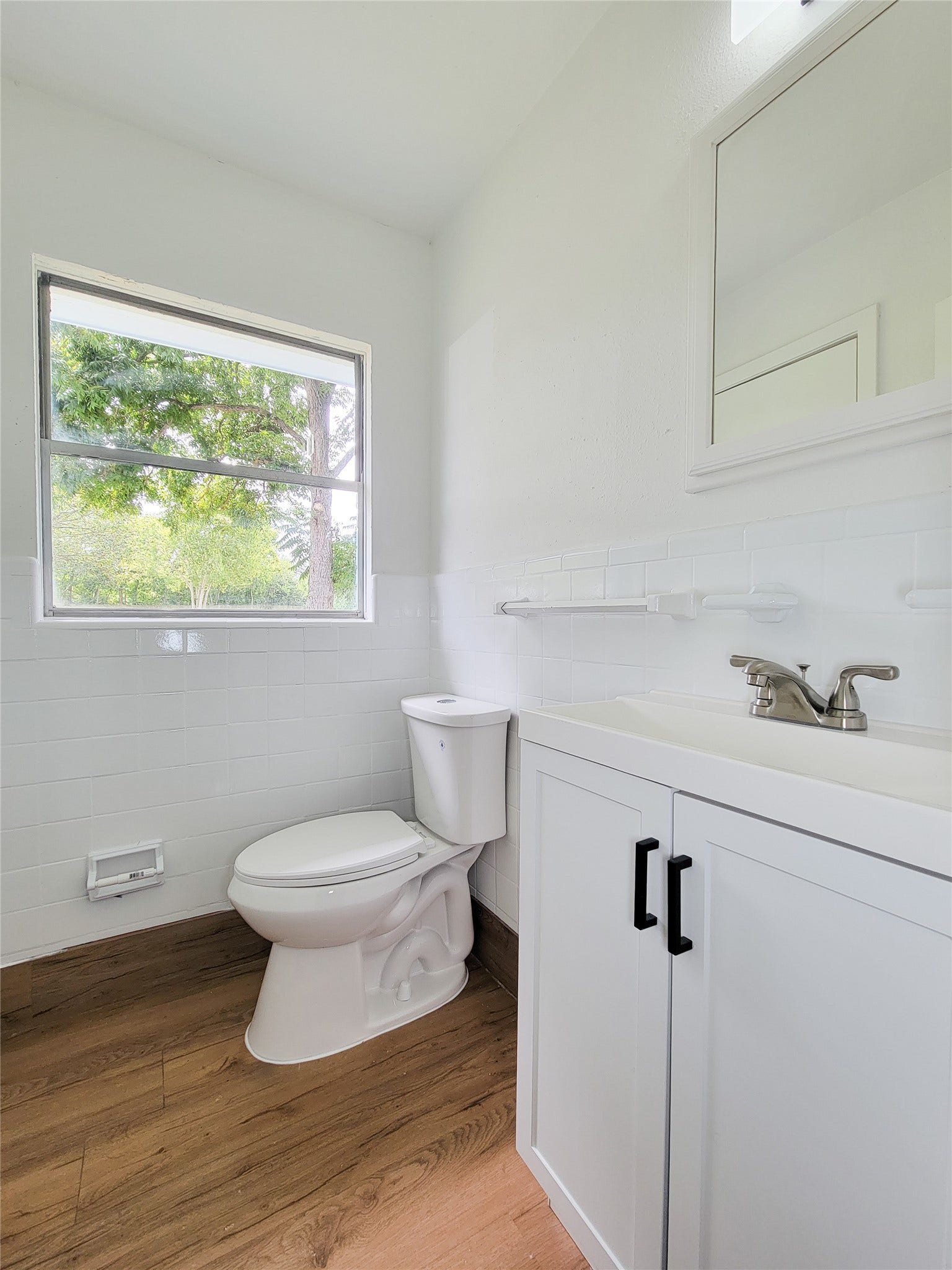 2605 W Dumble Street, Alvin, TX 77511 A bright bathroom featuring modern fixtures, a sleek vanity, and elegant wood flooring, all enhanced by a large window that invites natural light.