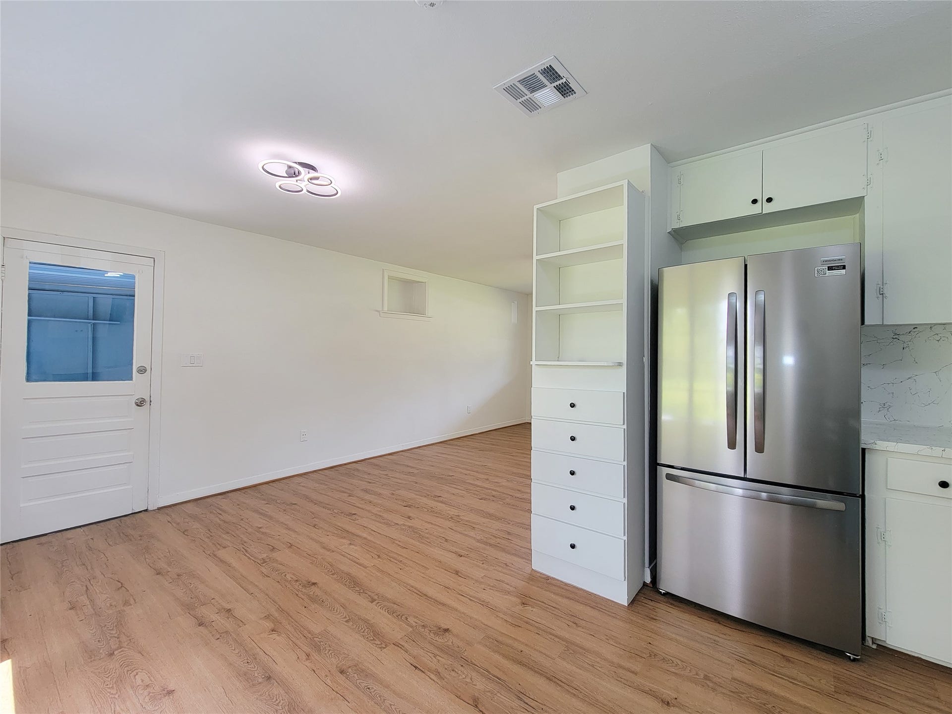 2605 W Dumble Street, Alvin, TX 77511 Experience the bright and airy kitchen, featuring modern stainless steel appliances, ample cabinet space, and elegant wood flooring, seamlessly flowing into a spacious adjacent area.