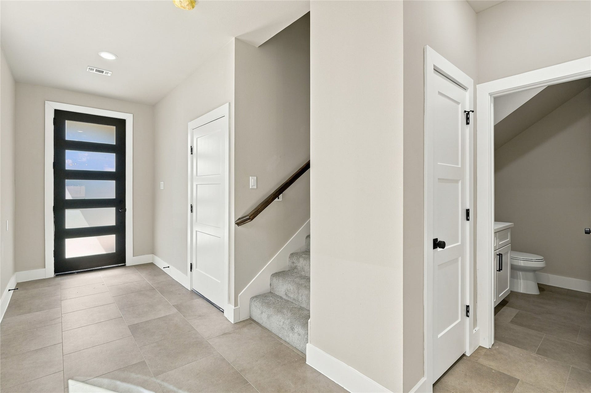 4313 Clover Street, #A/B, Houston, TX 77051 Modern entryway featuring a sleek glass-panel front door, elegant tile flooring, and convenient access to a half bathroom and staircase.