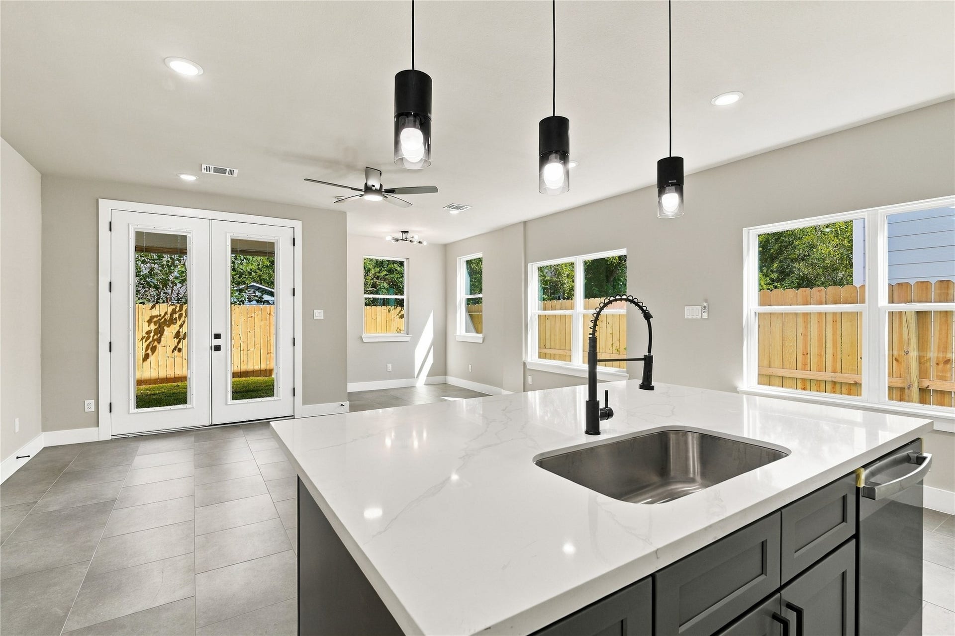 4313 Clover Street, #A/B, Houston, TX 77051 Modern open-concept kitchen and living area featuring sleek pendant lighting, a spacious island with a contemporary sink, and abundant natural light from large windows and French doors leading to a fenced backyard.