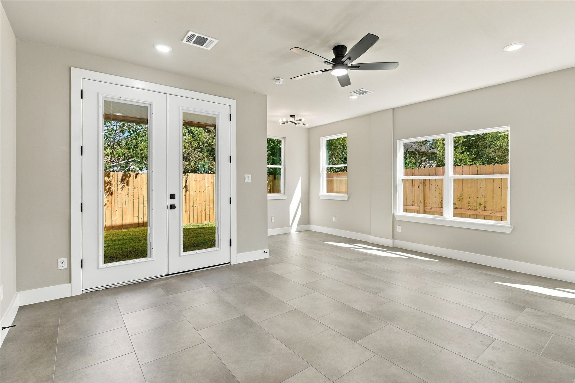 4313 Clover Street, #A/B, Houston, TX 77051 Bright and spacious living area featuring sleek tile flooring, a modern ceiling fan, and large windows that fill the room with natural light. Double glass doors open to a private backyard, perfect for indoor-outdoor living.