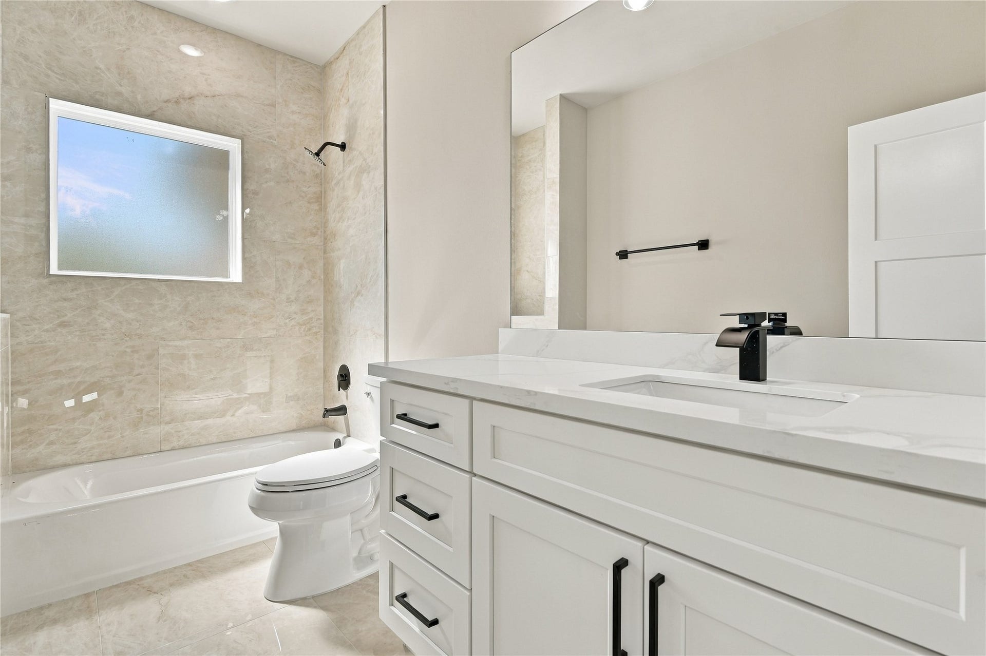 4313 Clover Street, #A/B, Houston, TX 77051 Bright, modern bathroom featuring a sleek white vanity with black fixtures, a spacious tub with elegant tile surround, and a large frosted window for natural light.
