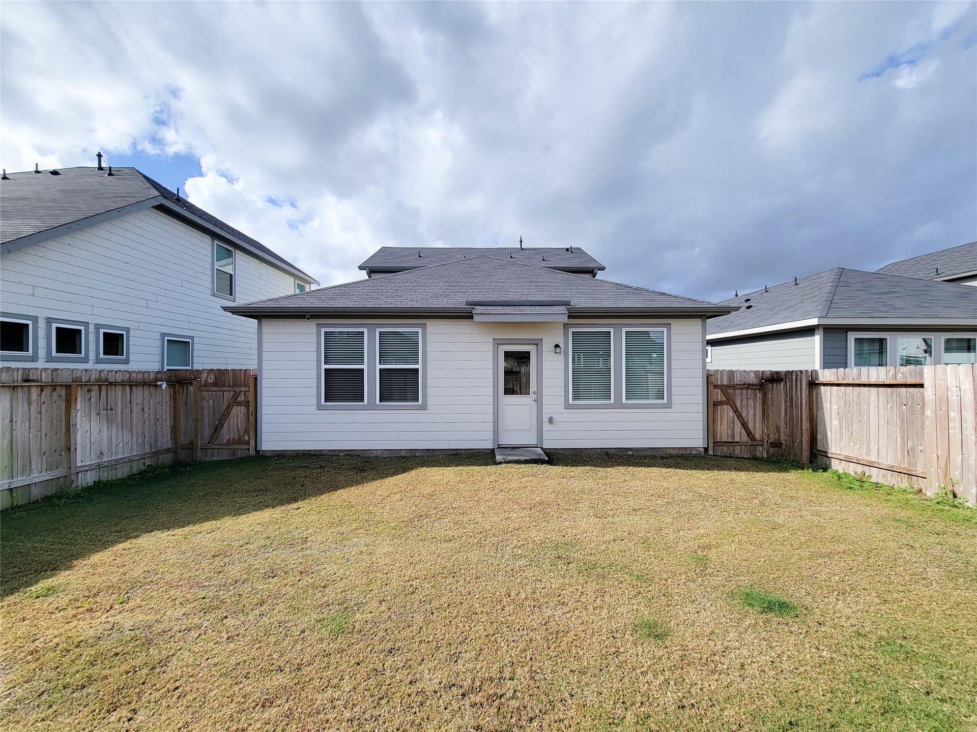 2719 Forest Retreat Lane, Missouri City, TX 77489 White siding and a dark roof. It has a small fenced backyard with a grassy area, a central back door, and two large windows. The space is enclosed by wooden fencing, providing privacy from neighboring homes.