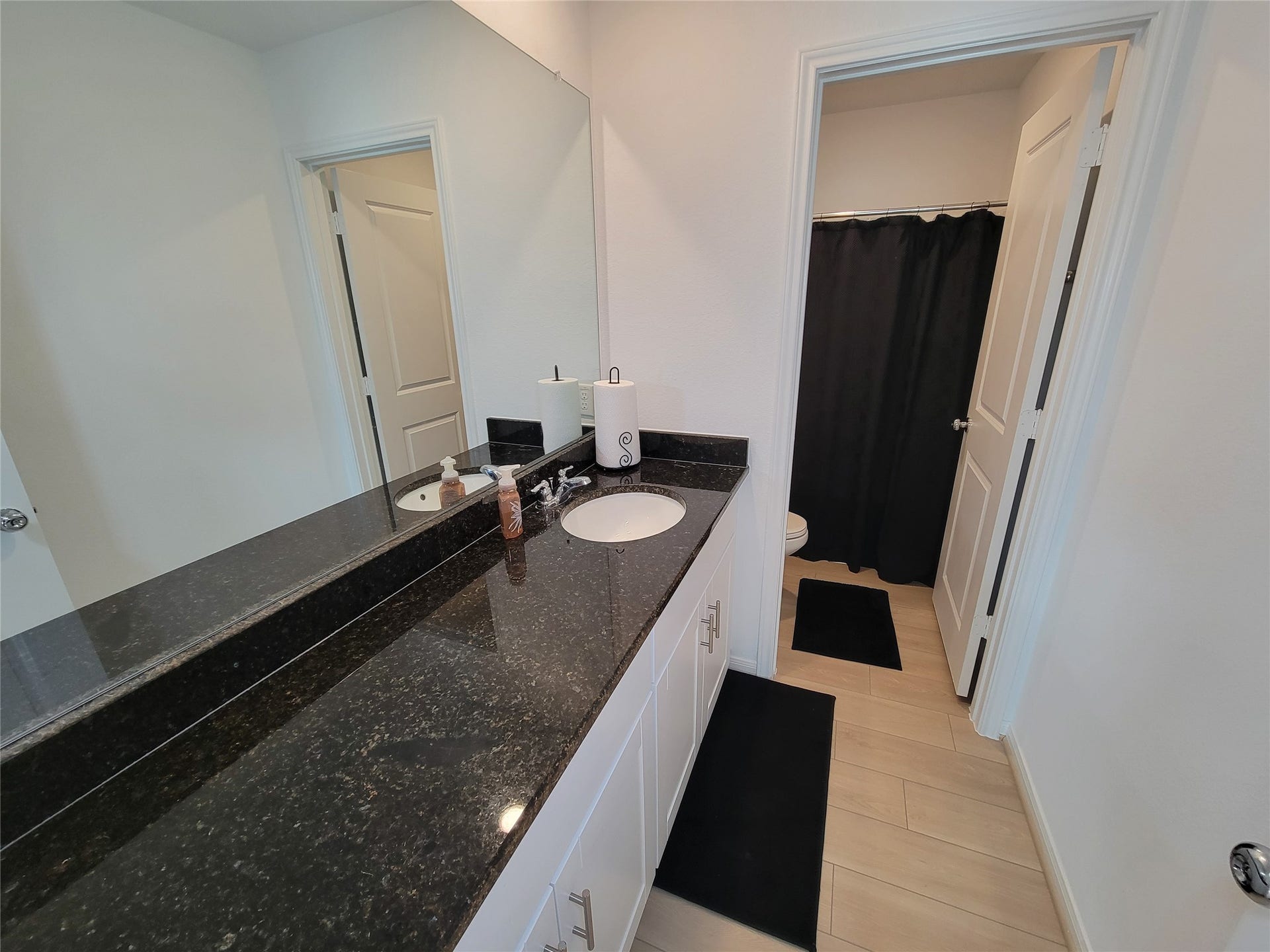 2719 Forest Retreat Lane, Missouri City, TX 77489 This bathroom features a sleek black granite countertop with dual sinks and modern fixtures. It includes a large mirror, light wood flooring, and a separate area with a shower and toilet, enhancing privacy.