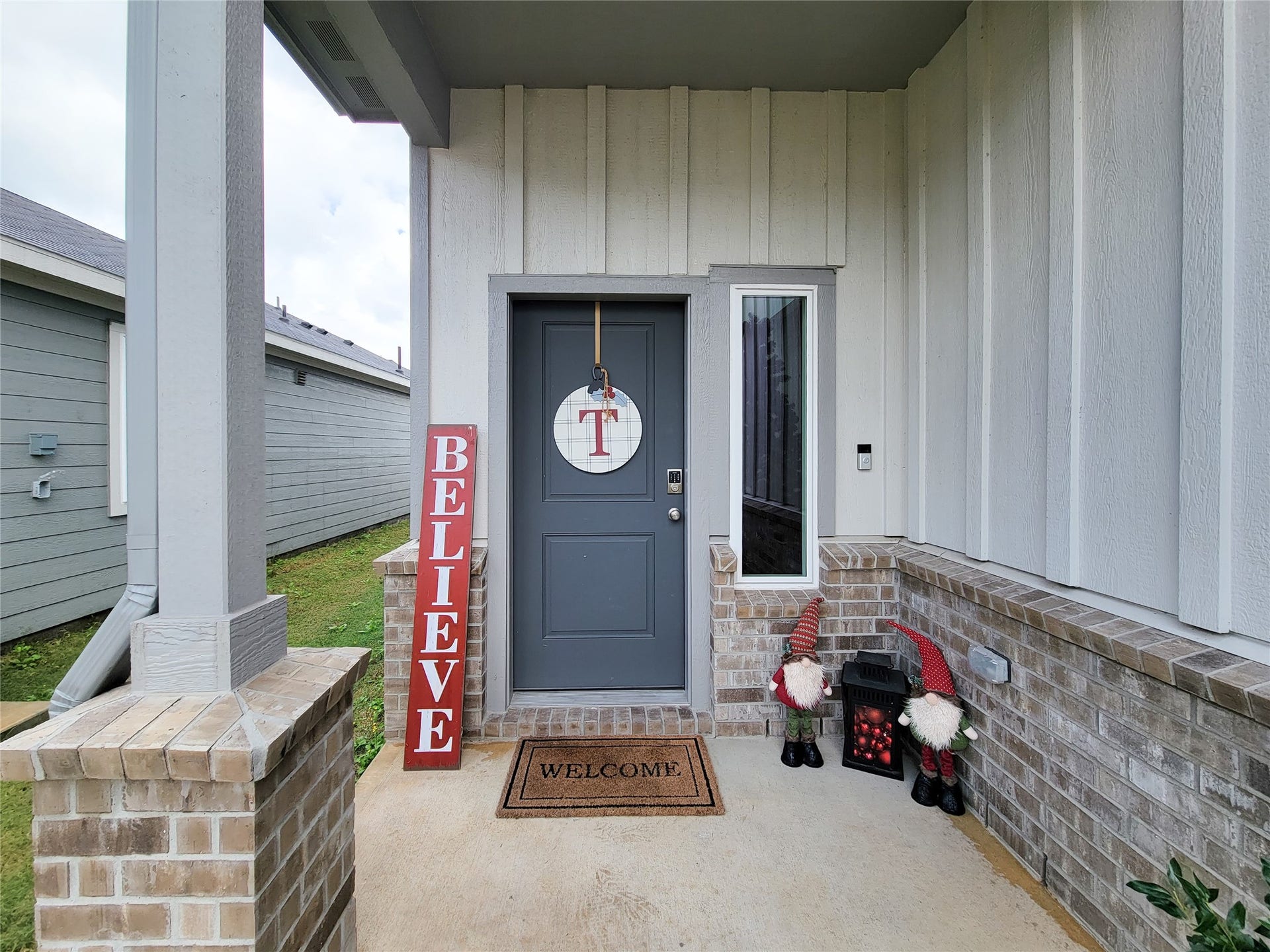 2719 Forest Retreat Lane, Missouri City, TX 77489 Charming front porch with a welcoming atmosphere, featuring a dark gray door, decorative signage, and festive gnomes. The brick and wood paneling add a cozy touch.