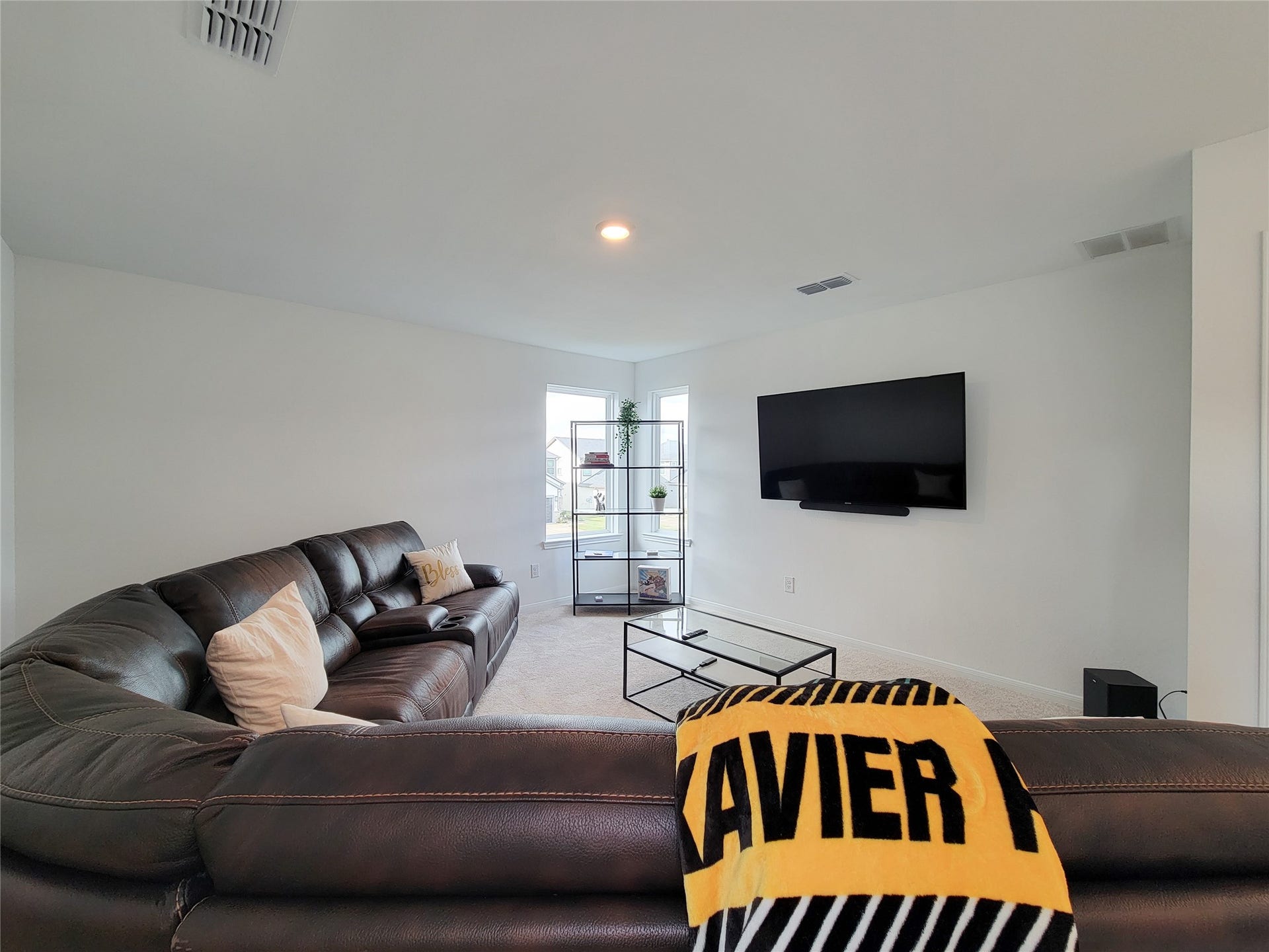 2719 Forest Retreat Lane, Missouri City, TX 77489 This spacious living room features a cozy, dark leather sectional, a wall-mounted TV, and a modern glass coffee table. A window brings in natural light, enhancing the room's airy feel. Perfect for relaxation and entertainment.