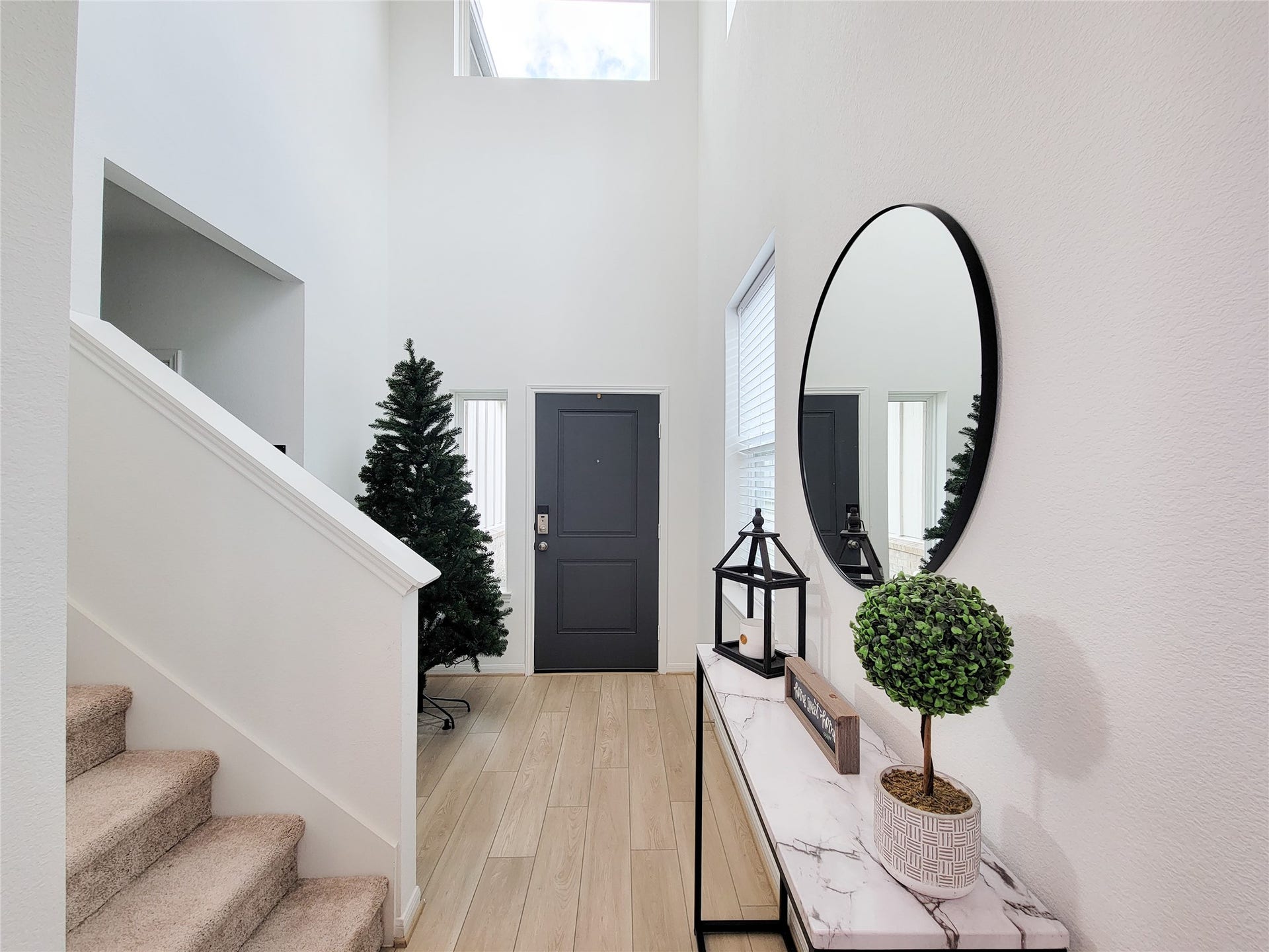 2719 Forest Retreat Lane, Missouri City, TX 77489 Bright entryway with high ceilings, modern decor, and a staircase. The space features wood-look flooring, a stylish console table with a round mirror, and ample natural light from a large window.