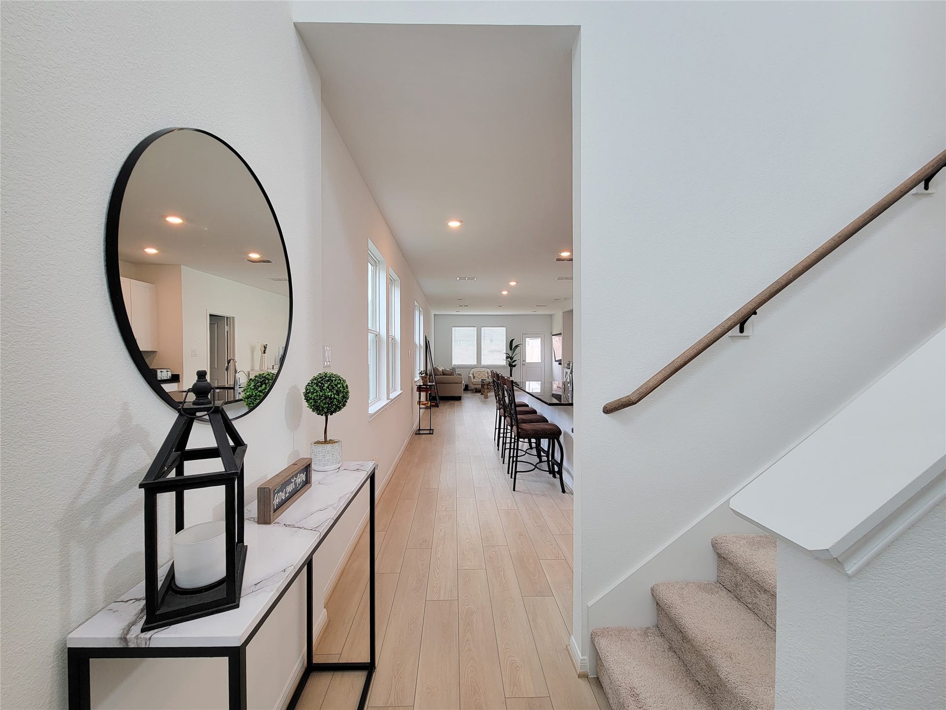 2719 Forest Retreat Lane, Missouri City, TX 77489 Entryway with modern decor, featuring a large round mirror and a sleek console table. The space leads into an open-plan living area with wooden flooring, ample natural light, and a glimpse of the dining and living rooms. A carpeted staircase is visible on the right.